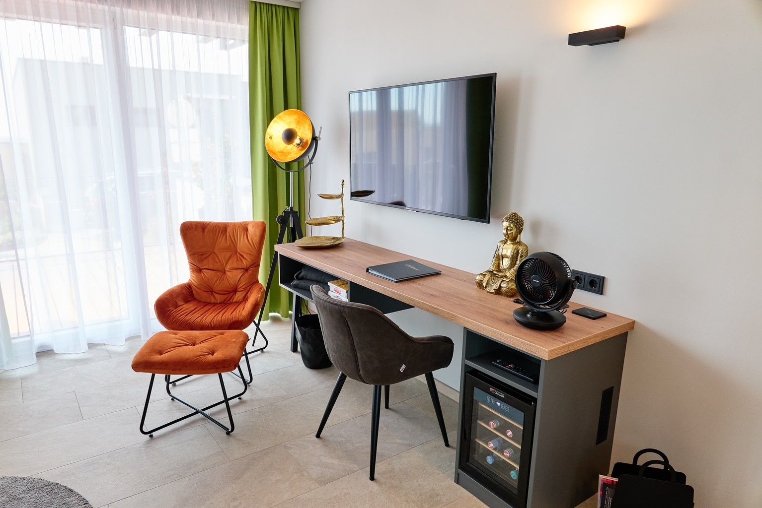 Wohnzimmer mit Sessel, Schreibtisch, Buddha-Statue und Fernseher.