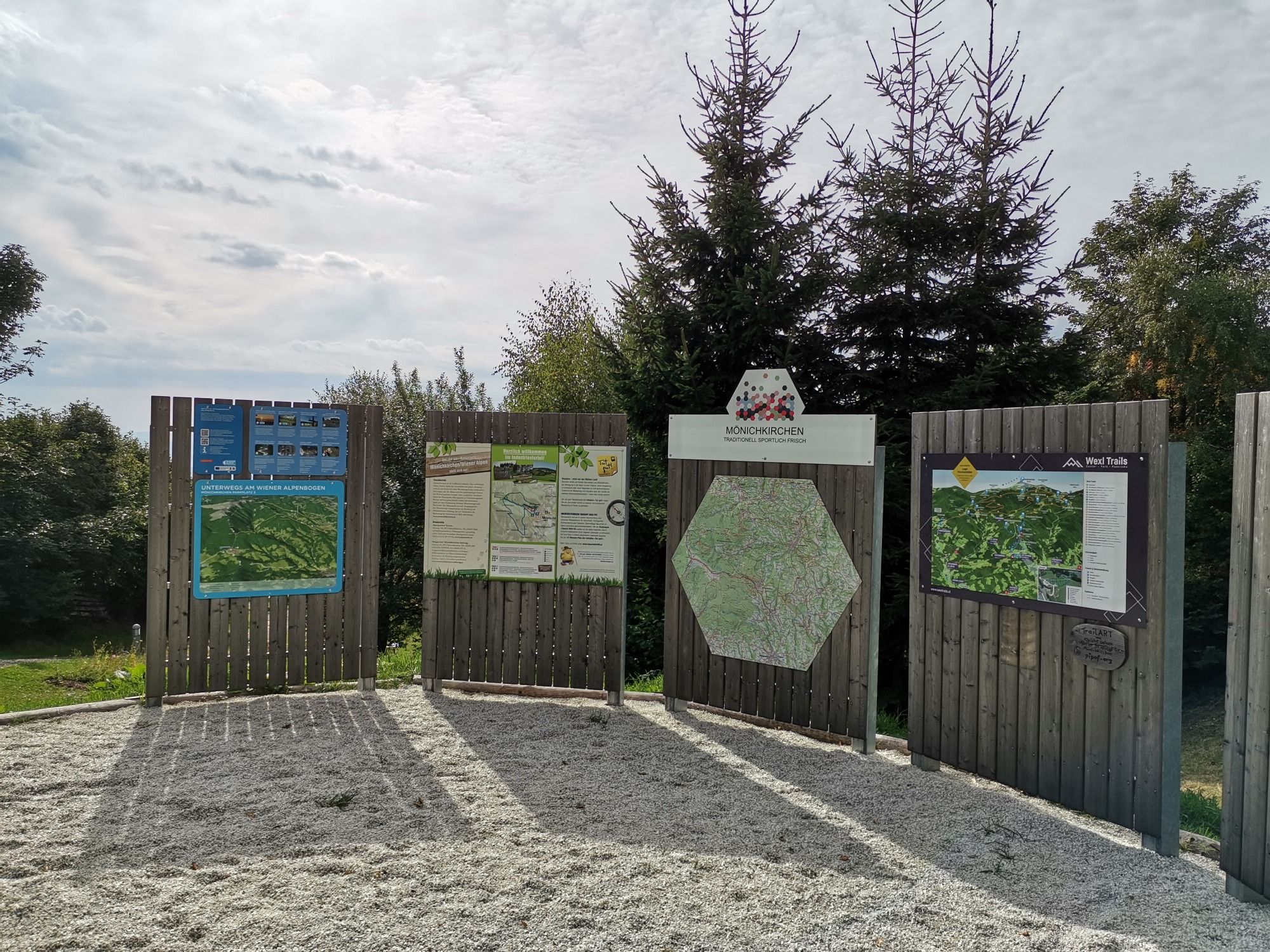 Informationstafeln am Wanderstartplatz in Mönichkirchen mit Karten und Hinweisen, umgeben von Bäumen.