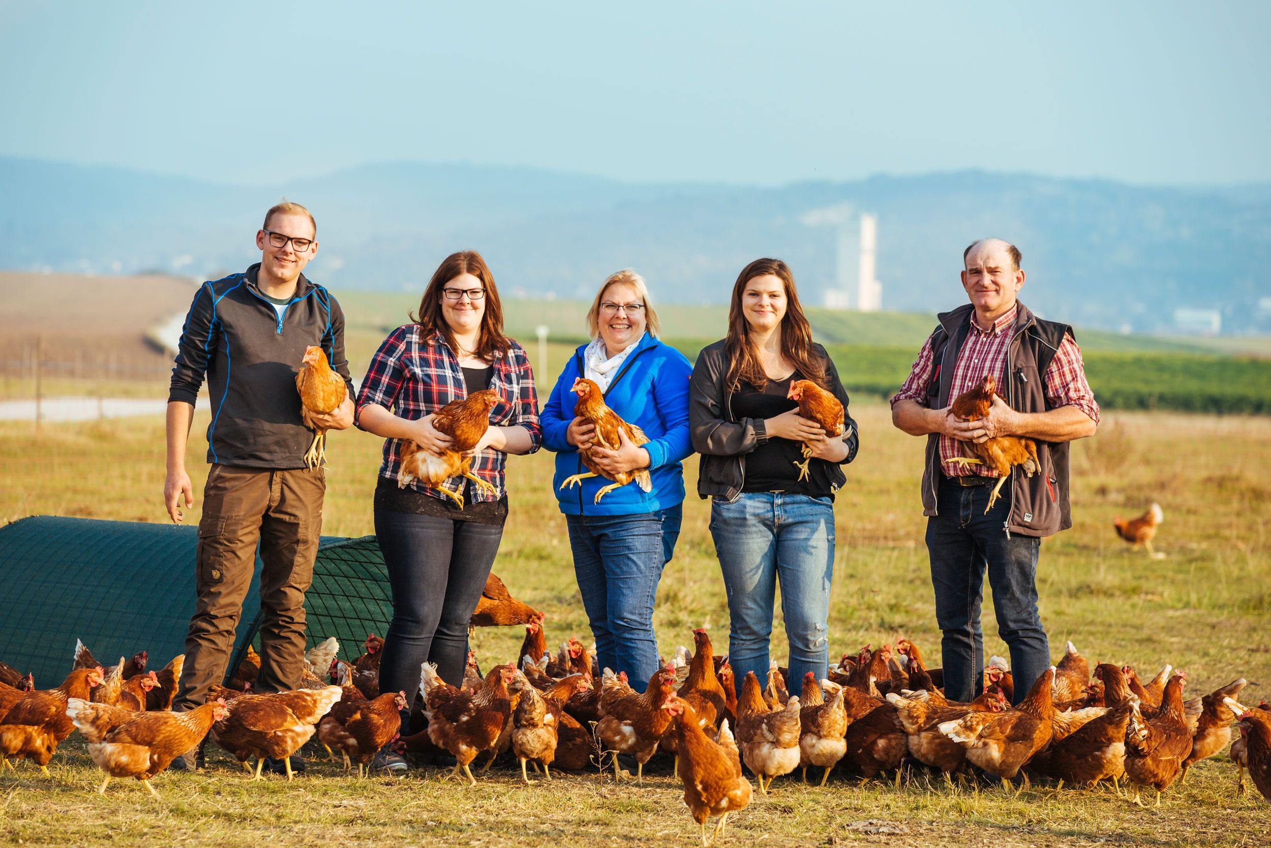 Eine Familie steht auf einem Feld mit Hühnern und hält einige in den Armen.
