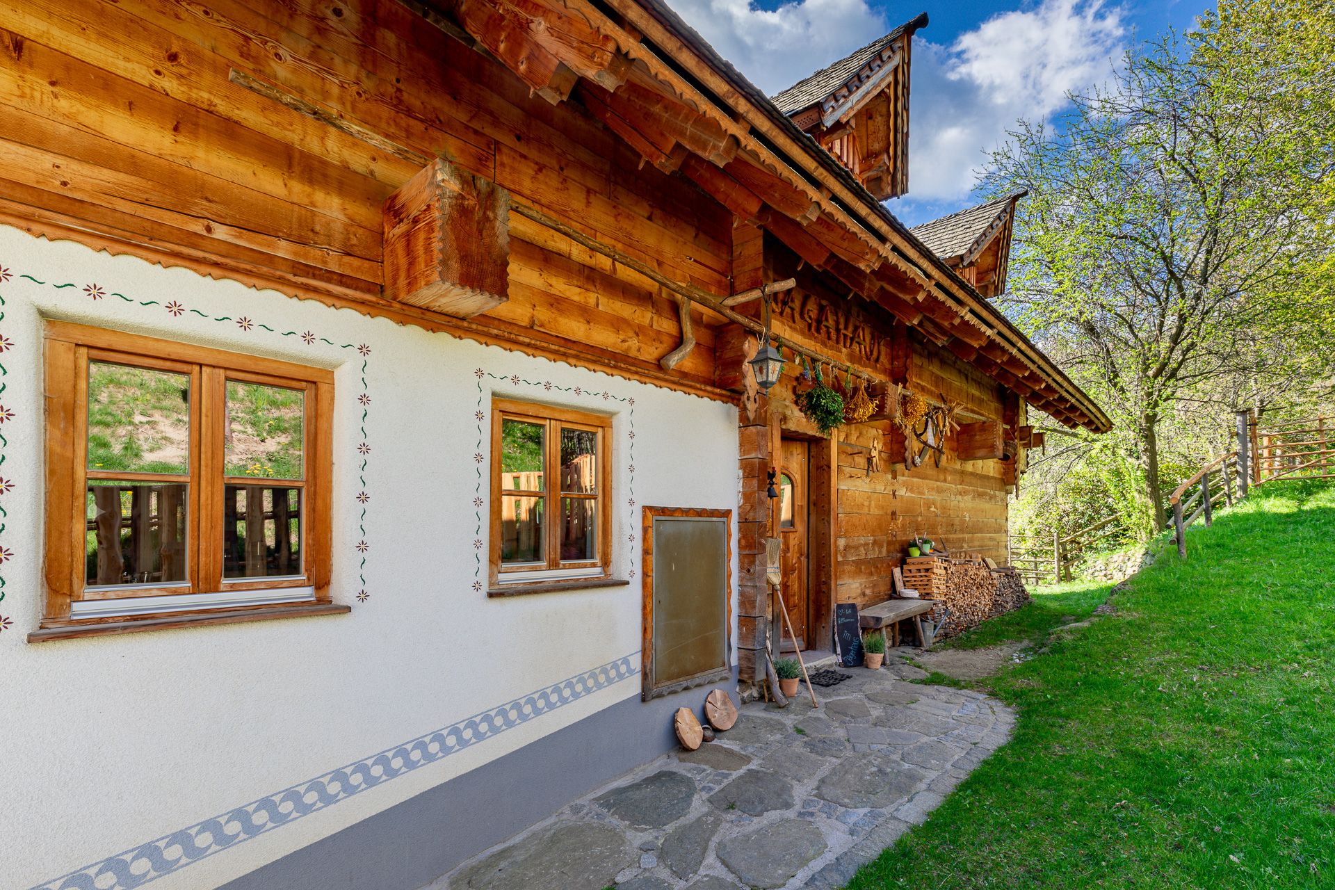 Traditionelles Haus mit viel Holz, dekorativen Fenstern und Deko neben einer grünen Wiese.