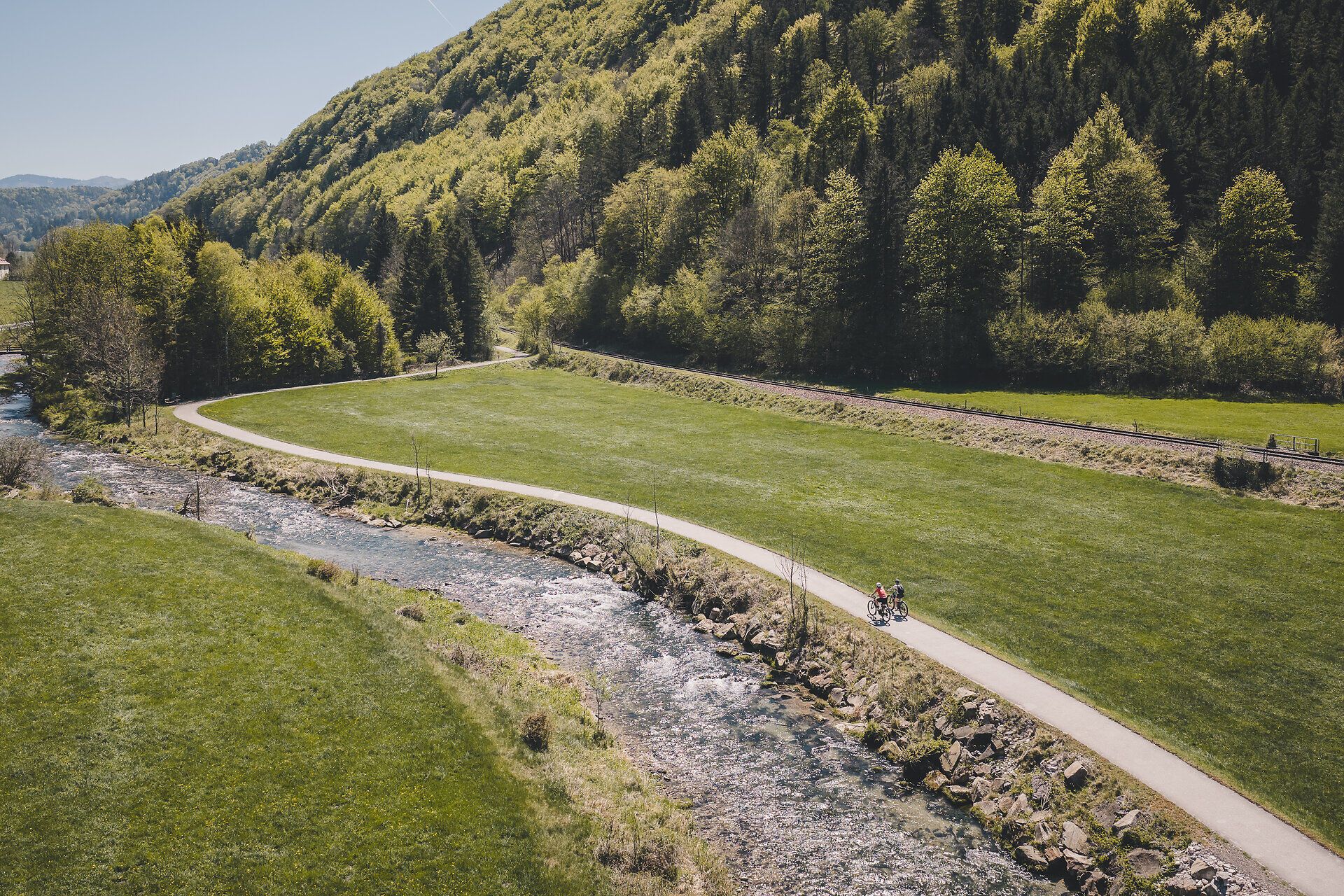 Zwei Radfahrerinnen fahren entlang des Radwegs neben einem Fluss.