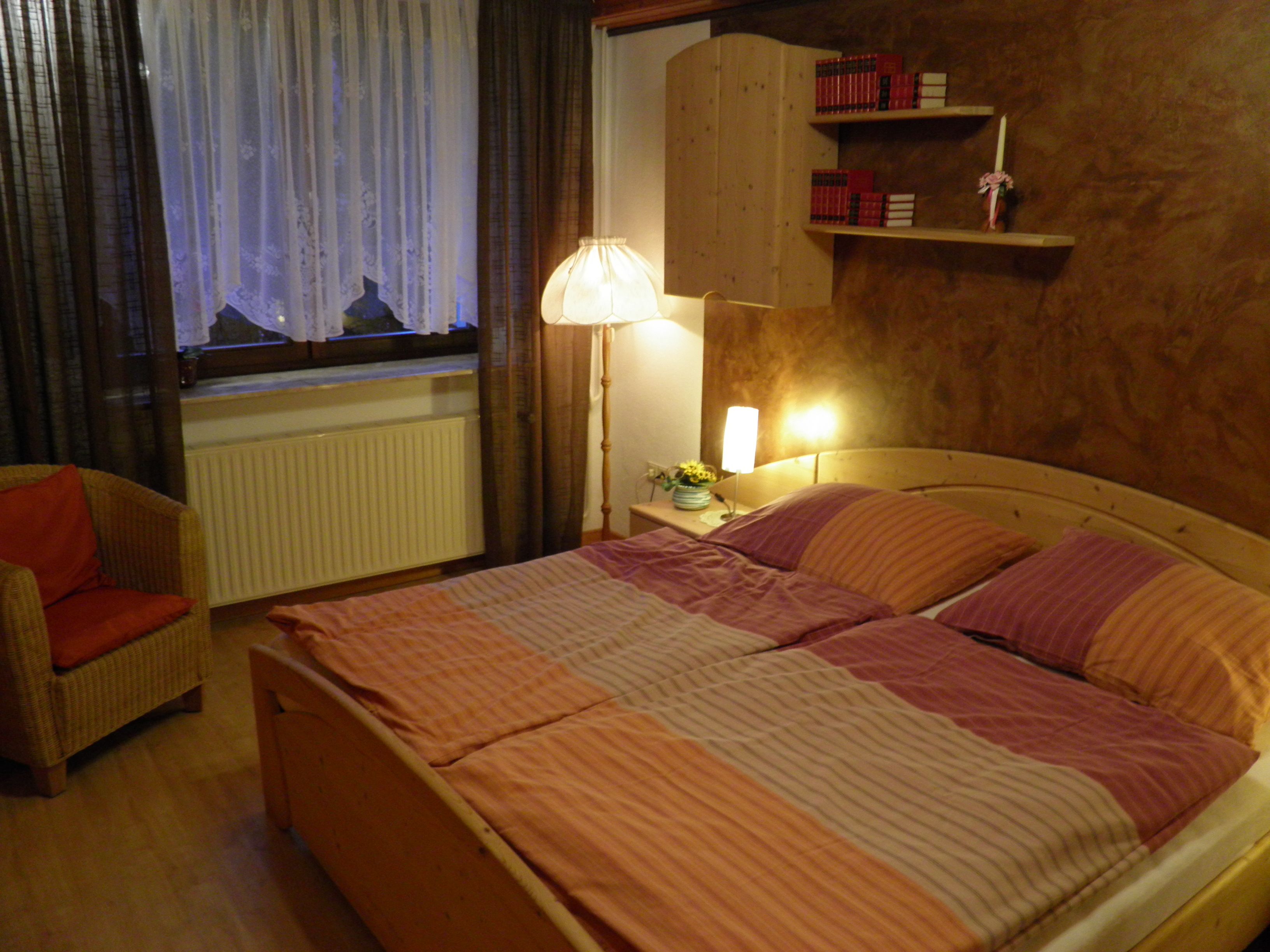 Gemütliches Schlafzimmer mit Doppelbett, Nachttischlampen, Bücherregal und Sessel.