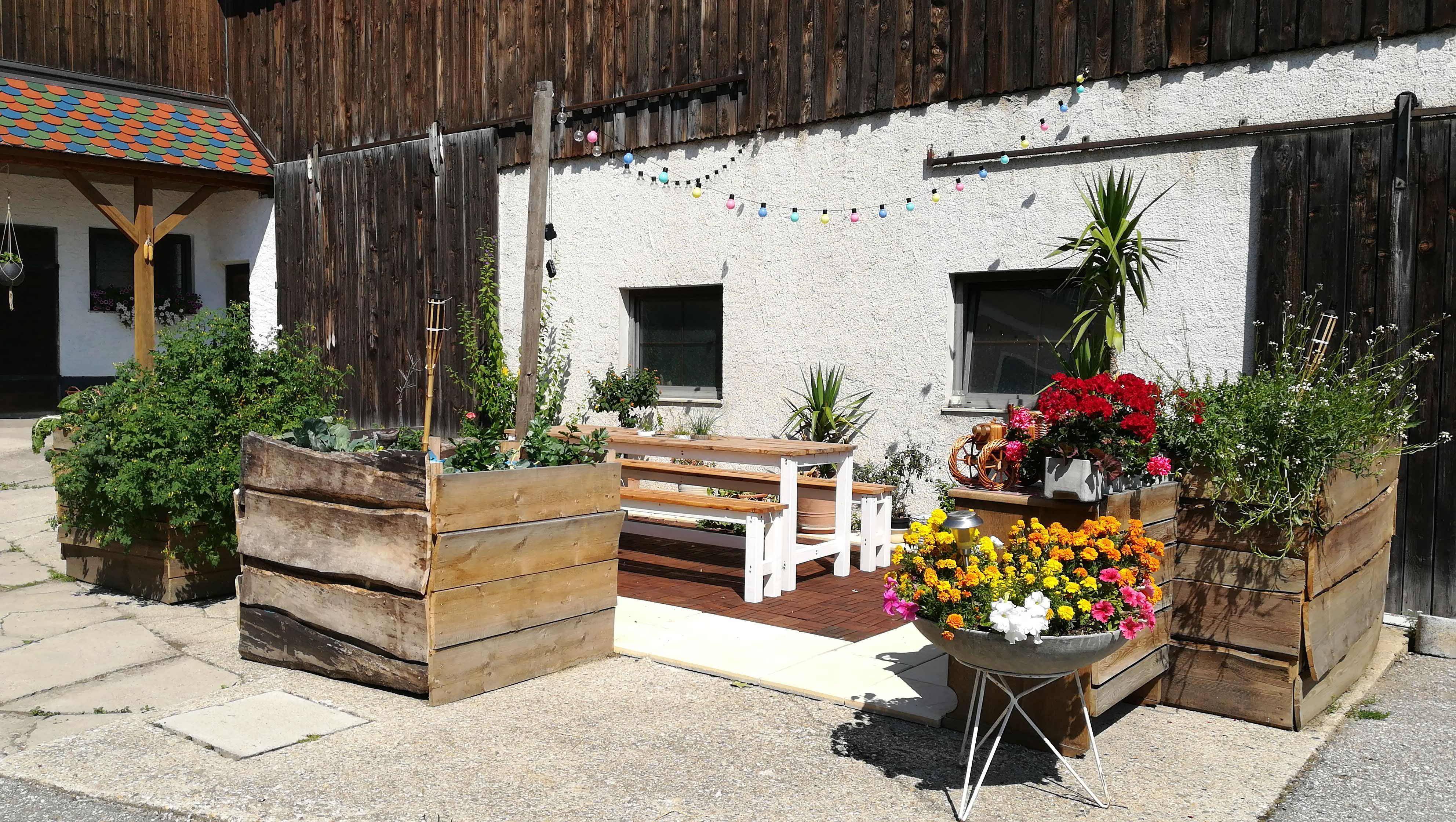 Ein Hof mit Holzbänken, Blumenkästen und bunter Lichterkette.