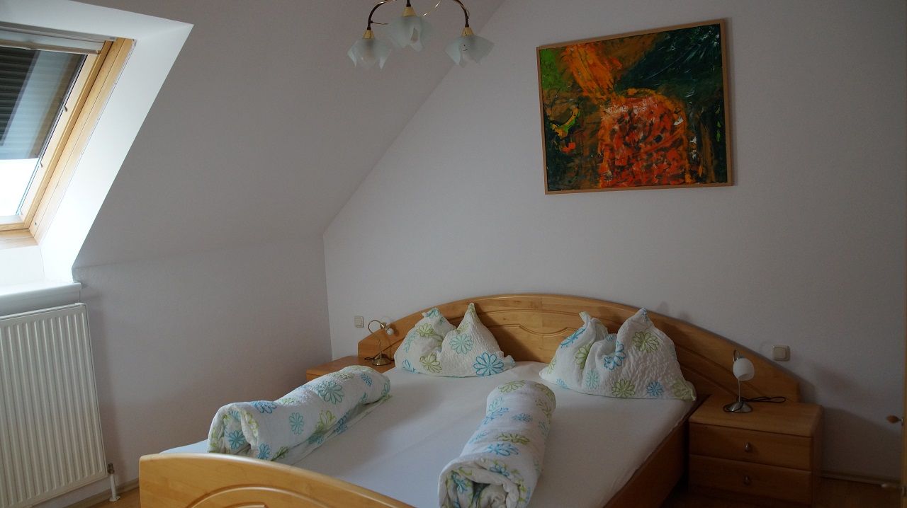 Schlafzimmer mit Doppelbett, Dachfenster und abstraktem Gemälde an der Wand.