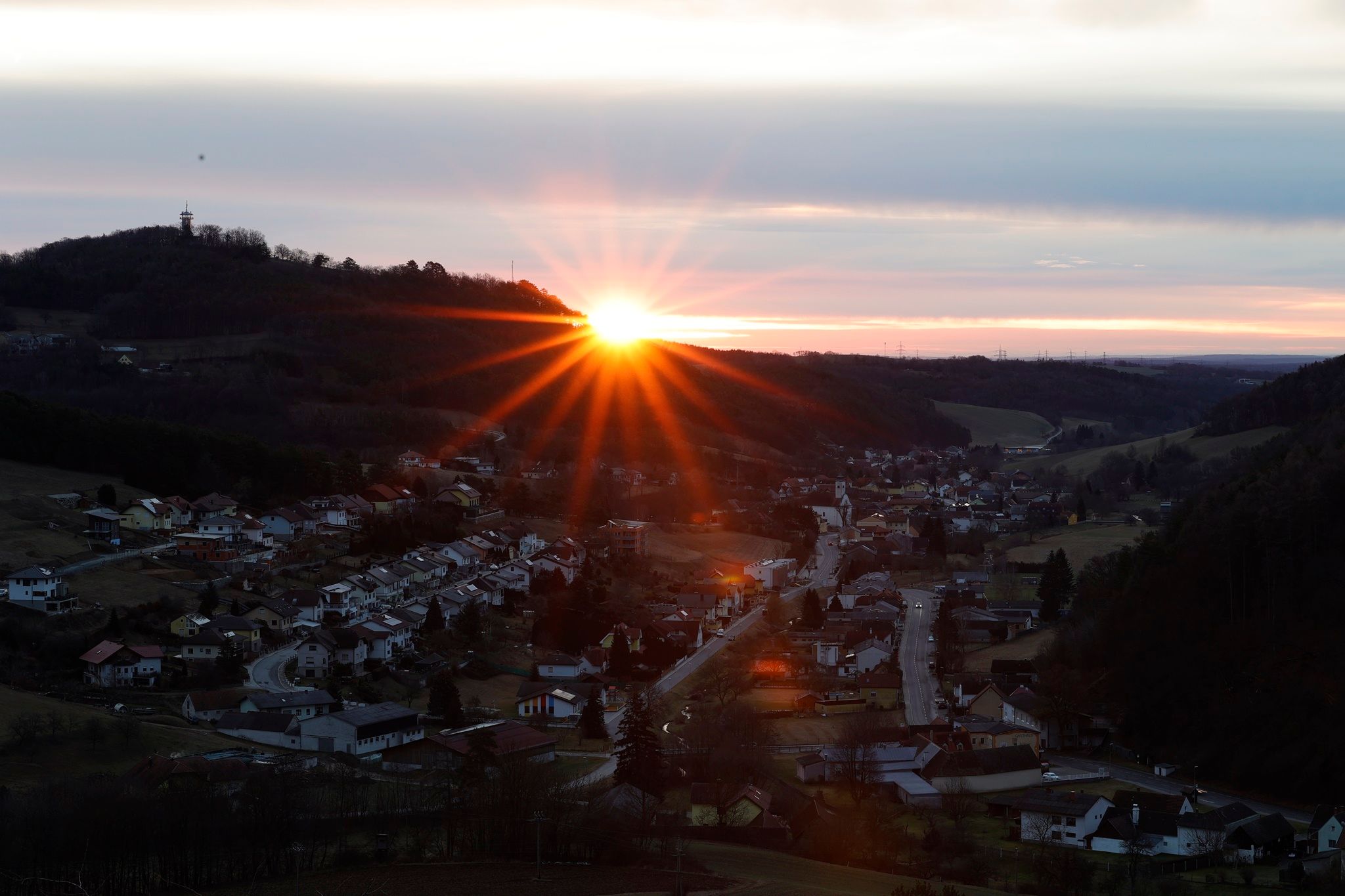 Sonnenaufgang hinter einem Hügel mit einem Dorf im Vordergrund.