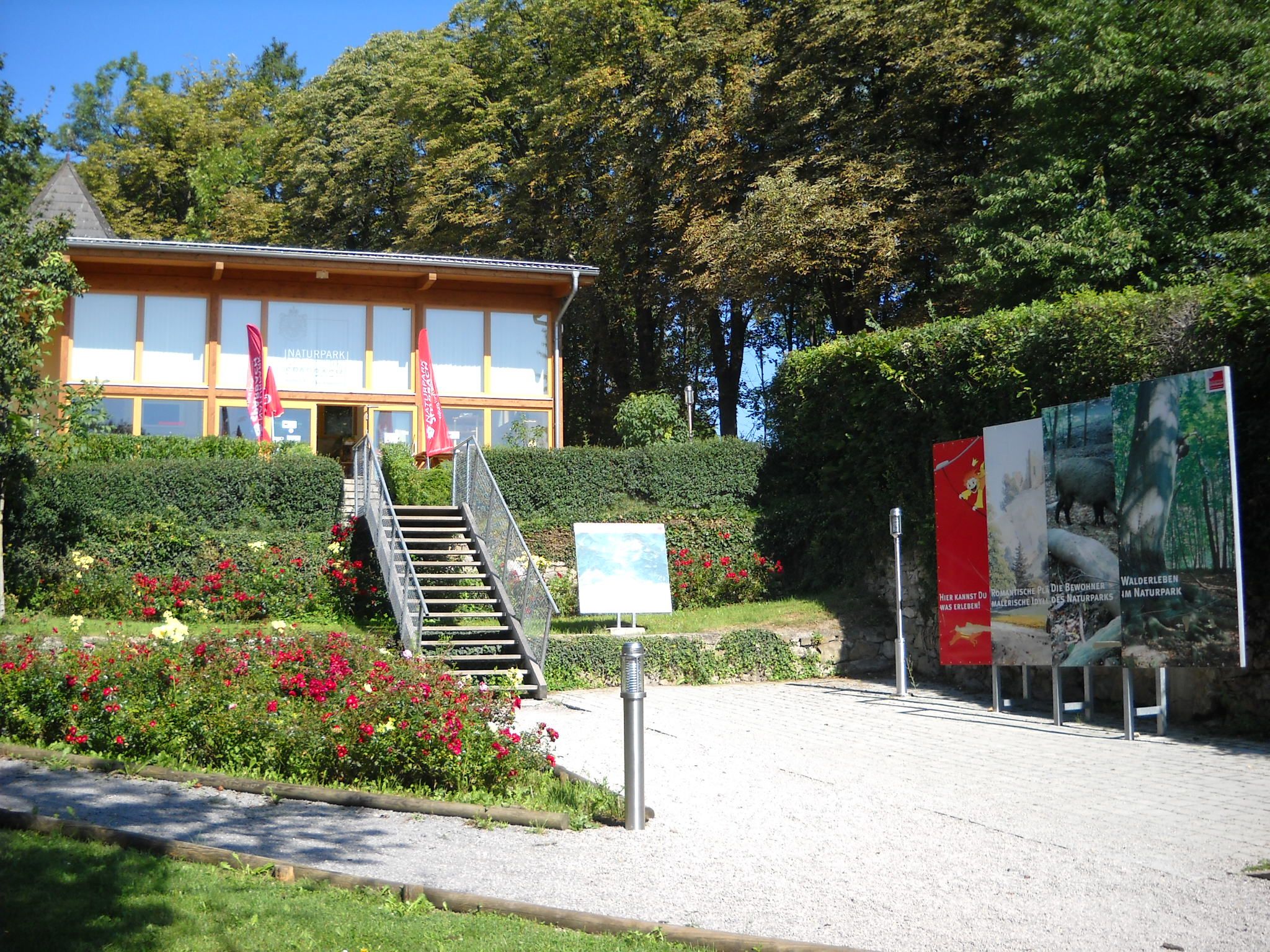 Eingang des Naturparks Sparbach mit Treppe, Blumenbeeten und Infotafeln.