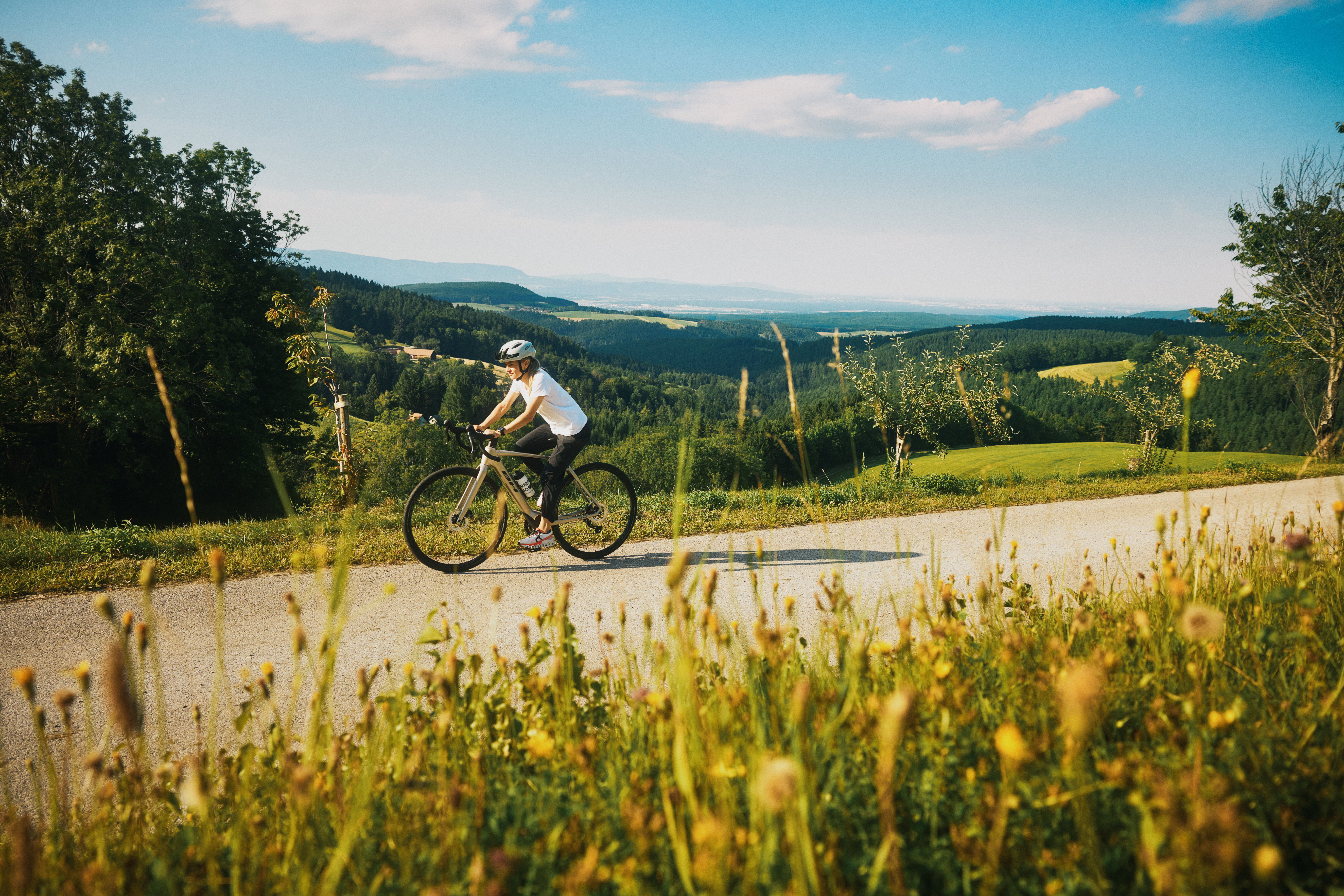 Eine Person fährt mit einem Fahrrad auf einer ländlichen Straße, im Hintergrund weiter Aussicht.