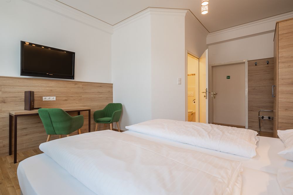 Hotelzimmer mit Doppelbett, grüne Stühle, Schreibtisch und Fernseher.