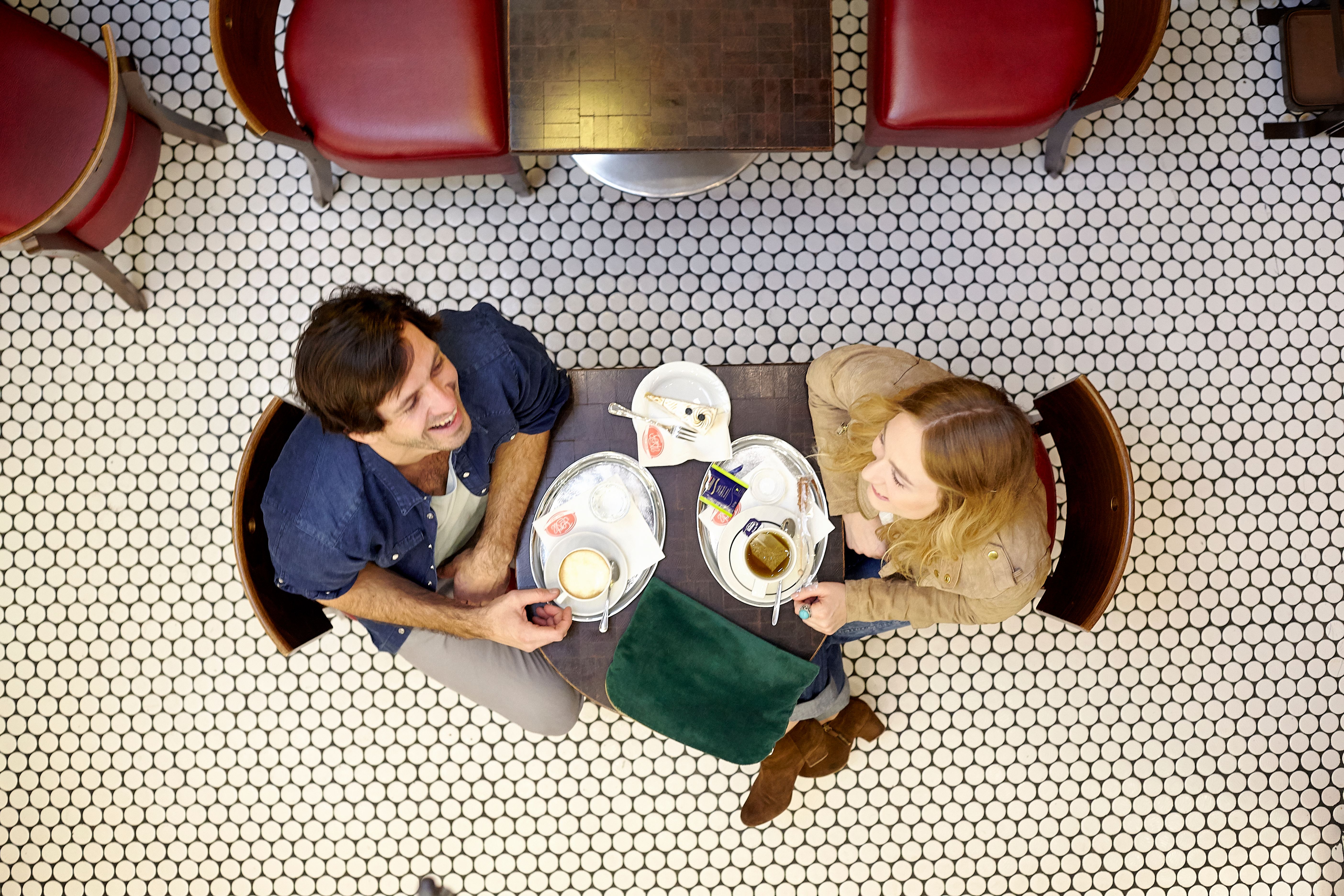 Ein belebter Hauptplatz mit Cafés und Geschäften, umgeben von historischen Gebäuden. Menschen sitzen draußen, ein Radfahrer fährt vorbei. Blauer Himmel mit Wolken.