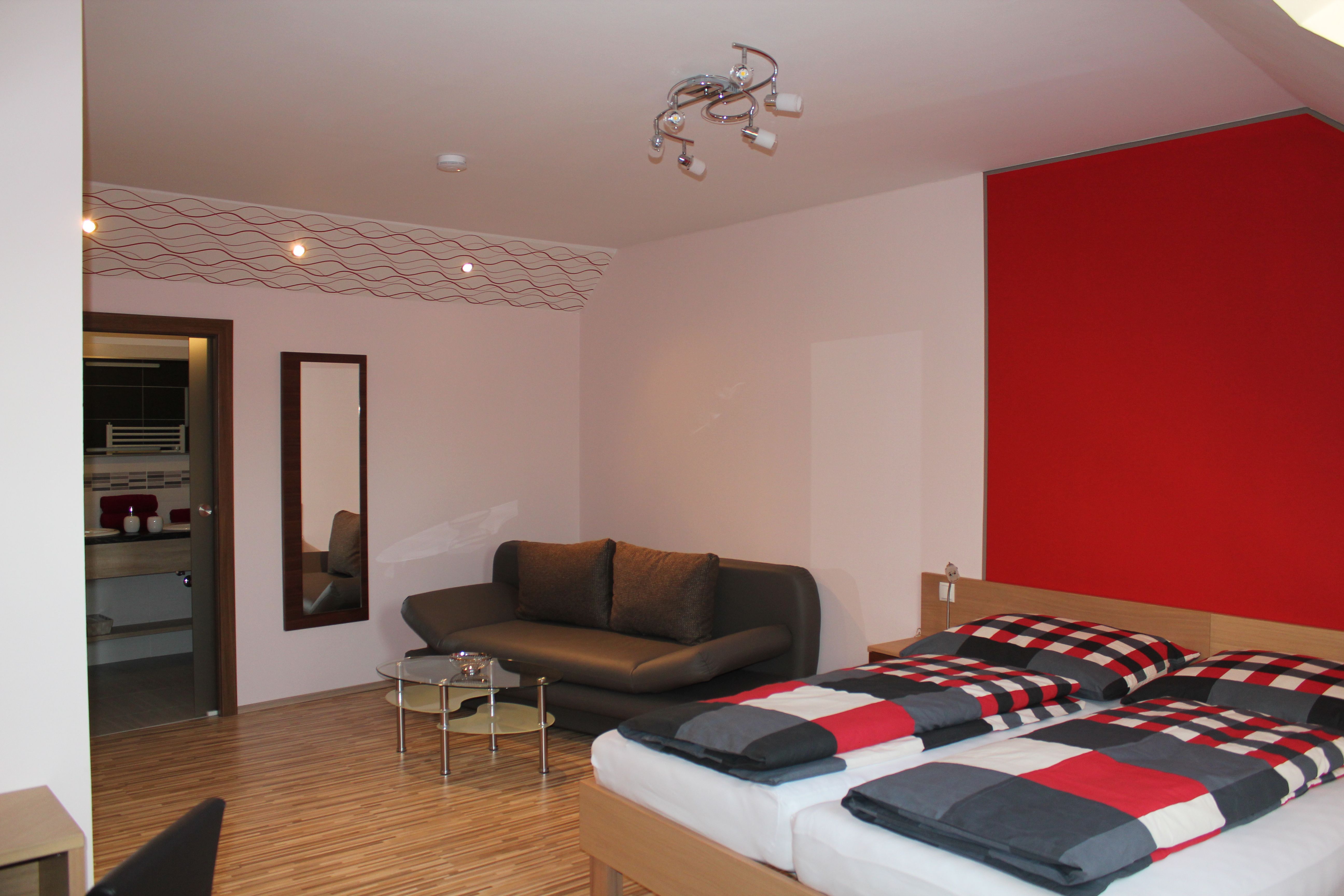 Modern eingerichtetes Gästezimmer mit Doppelbett, Sofa und kleinem Tisch.