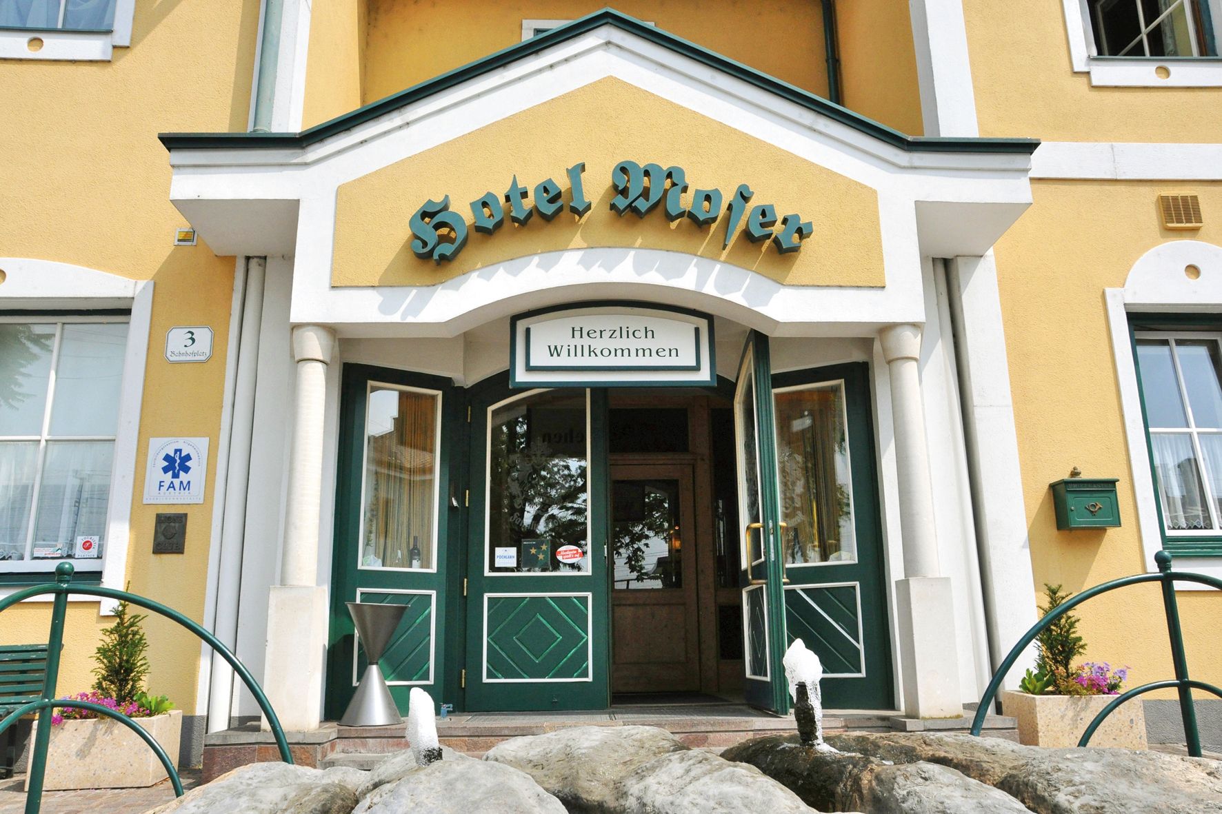 Eingang des Hotel Moser mit gelber Fassade und grünen Türen.