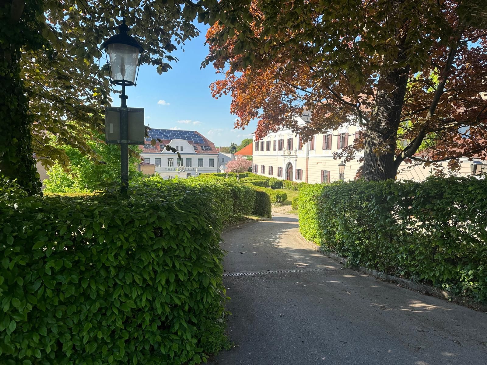 Ansicht eines Schlosses in Großrußbach, umgeben von Bäumen und Hecken, mit einer Laterne im Vordergrund.