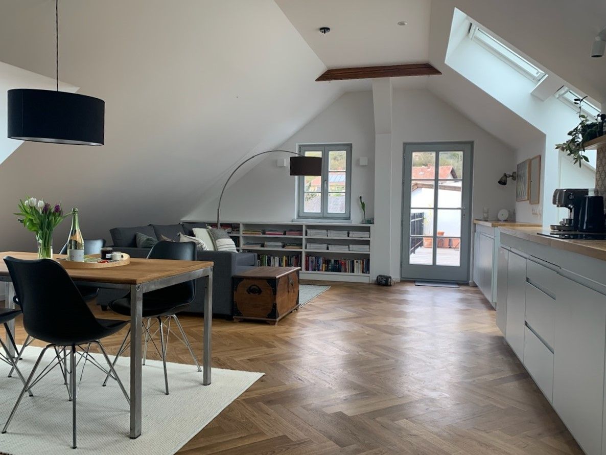 Modernes Dachgeschoss-Apartment mit Holzboden, Esstisch, Sofa und Zugang zu einem Balkon.