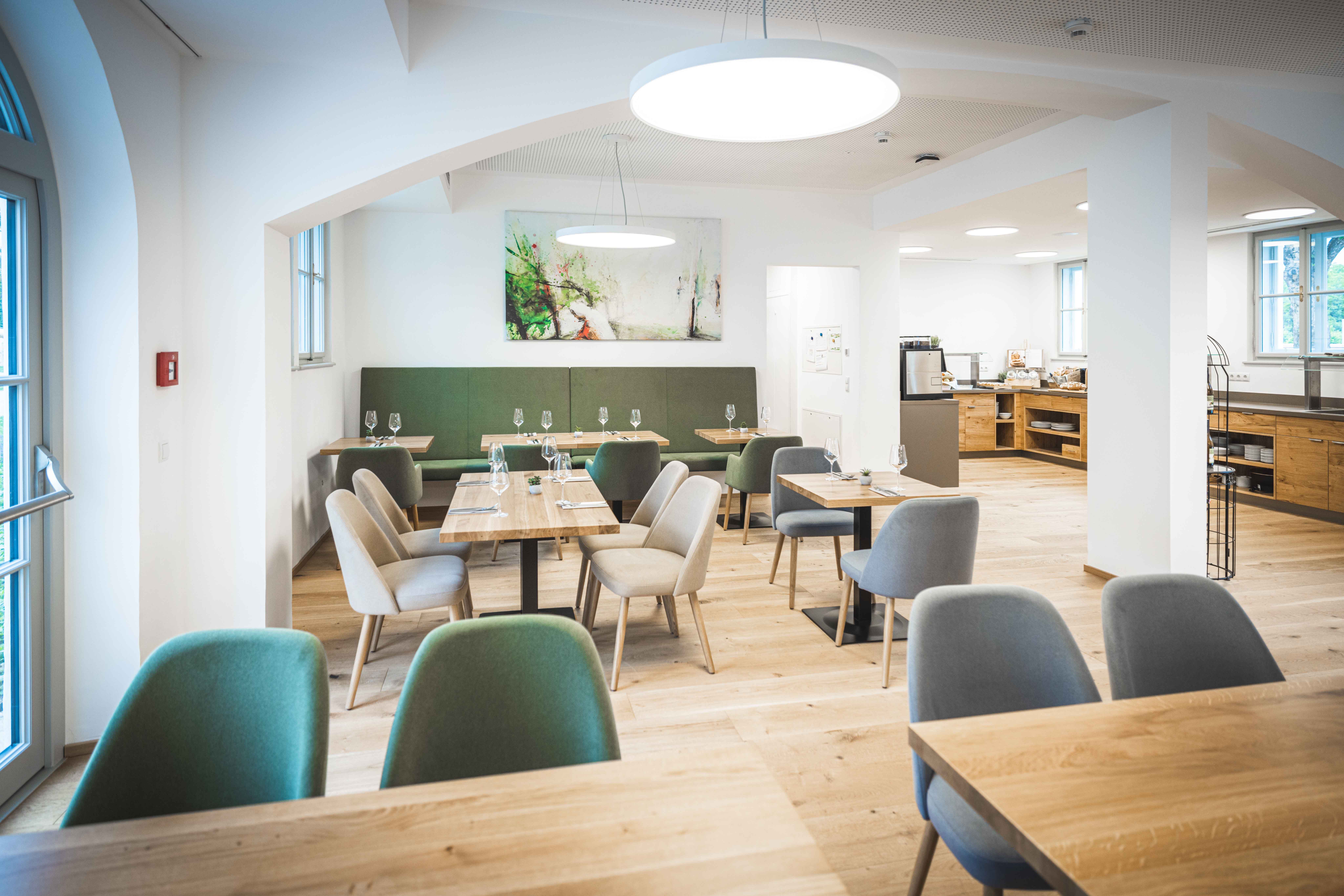 Modernes Restaurant mit Holztischen und gepolsterten Stühlen, helle Beleuchtung und Kunst an der Wand.