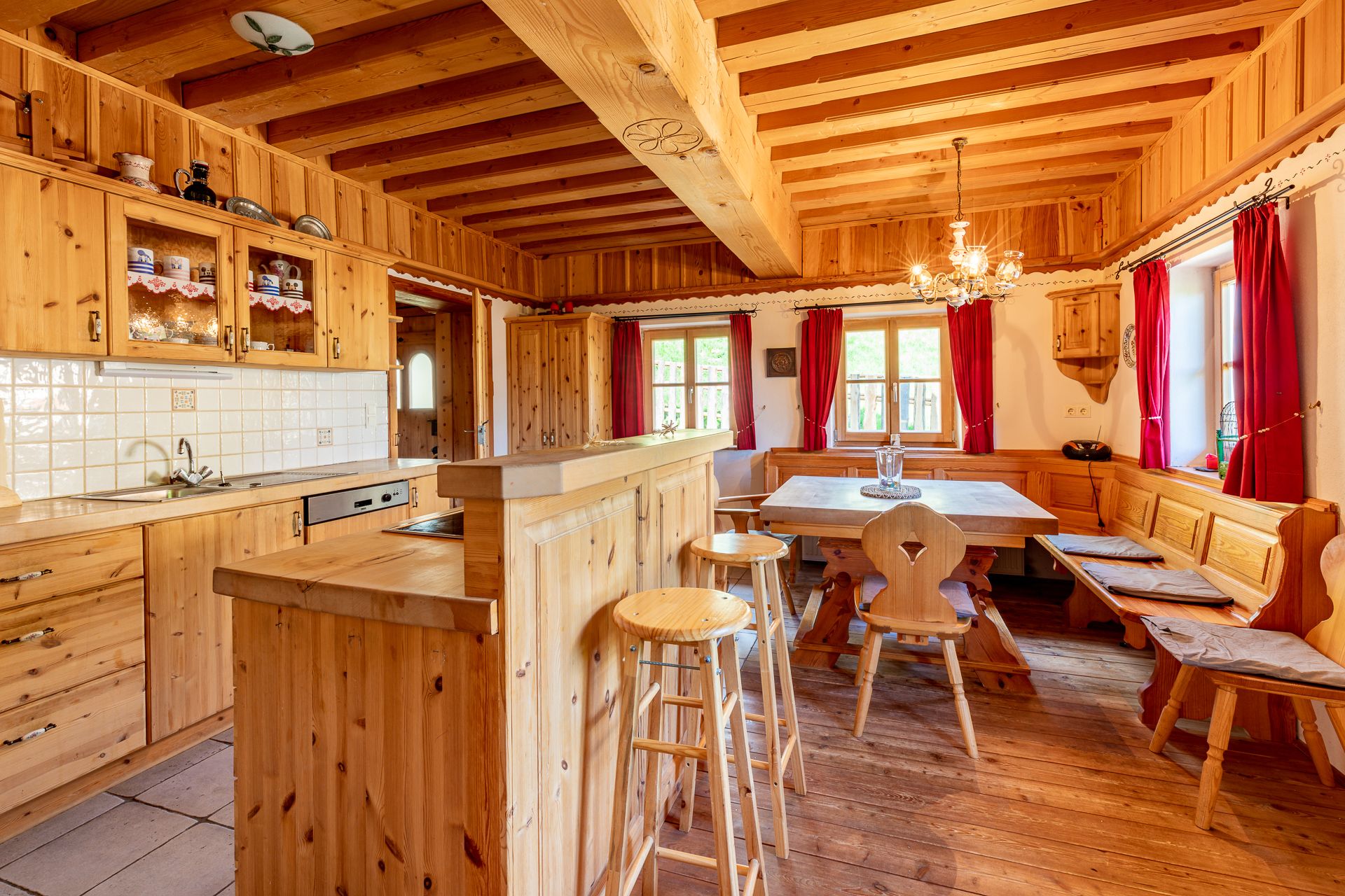 Traditionelle Holzküche mit Esstisch, Bank, Stühlen und roten Vorhängen.