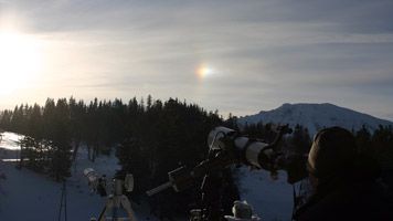 Teleskope auf einer verschneiten Bergstation mit Sonnenhalo im Hintergrund.