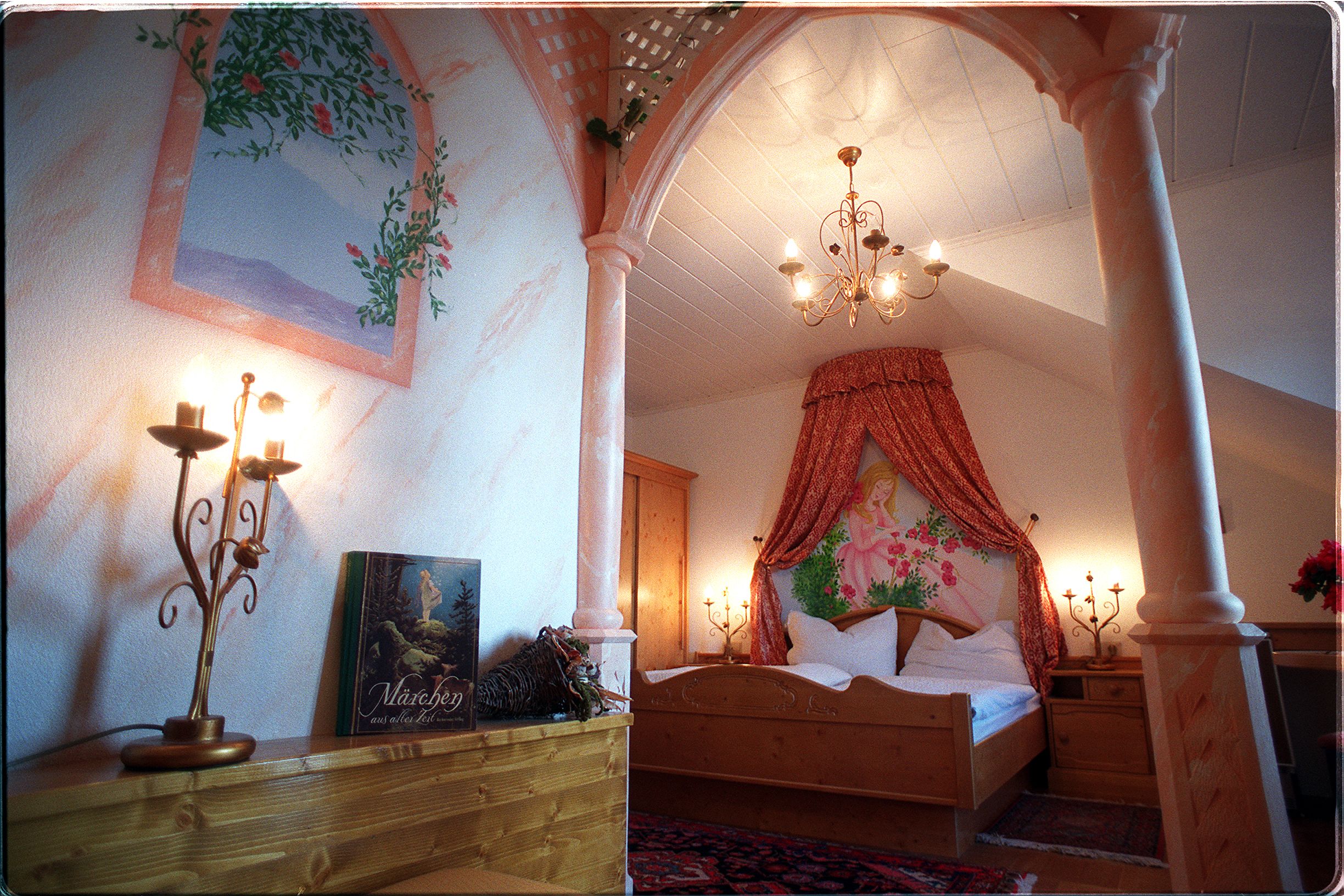 Ein romantisch dekoriertes Schlafzimmer mit Baldachin, Kerzenleuchtern und einem Märchenbuch auf einem Regal.