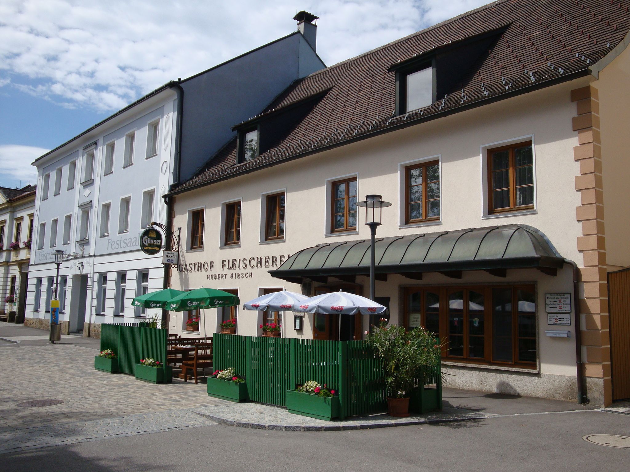 Gasthaus Fleischerei Hirsch mit Außenterrasse und Sonnenschirmen.