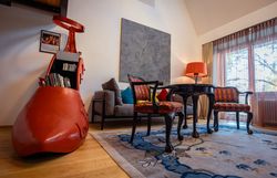 Ein stilvoll eingerichtetes Hotelzimmer mit einem großen roten Schuh als Bücherregal, antiken Stühlen, einem Tisch und einer Stehlampe.