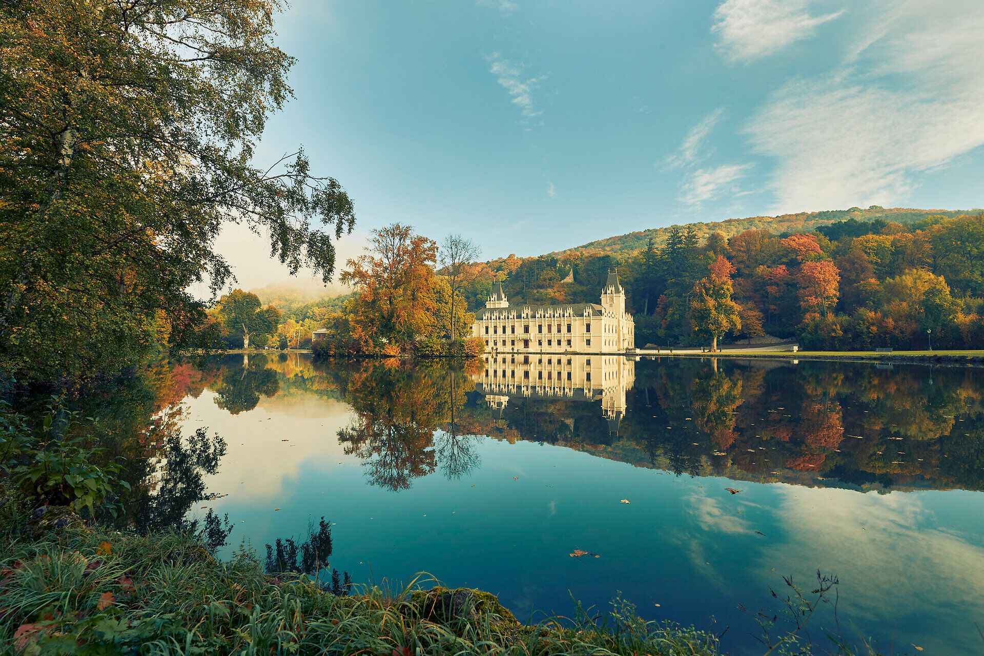 Umgeben von bunten Herbstblättern spiegelt sich das majestätische Schloss Hernstein im ruhigen Wasser des Sees wider. Die sanften Hügel im Hintergrund laden zu einem entspannenden Spaziergang ein, während die frische Luft die Sinne belebt.
