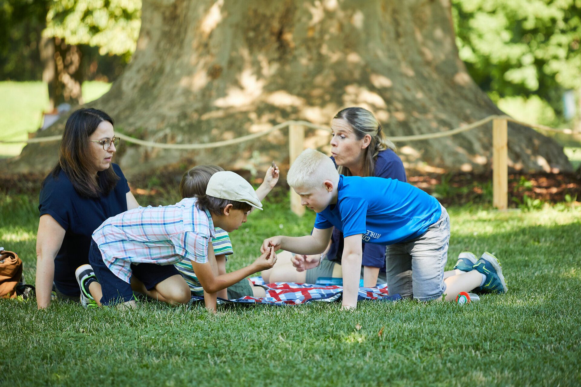 Inmitten der grünen Wiesen und schattenspendenden Bäume versammeln sich Familienmitglieder, um gemeinsam unvergessliche Momente zu erleben. Die Kinder spielen fröhlich miteinander, während die Erwachsenen entspannt im Gras sitzen und die harmonische Atmosphäre genießen. Ein perfekter Tag für ein Familienshooting, um die Schönheit der Natur und die Freude am Zusammensein festzuhalten.