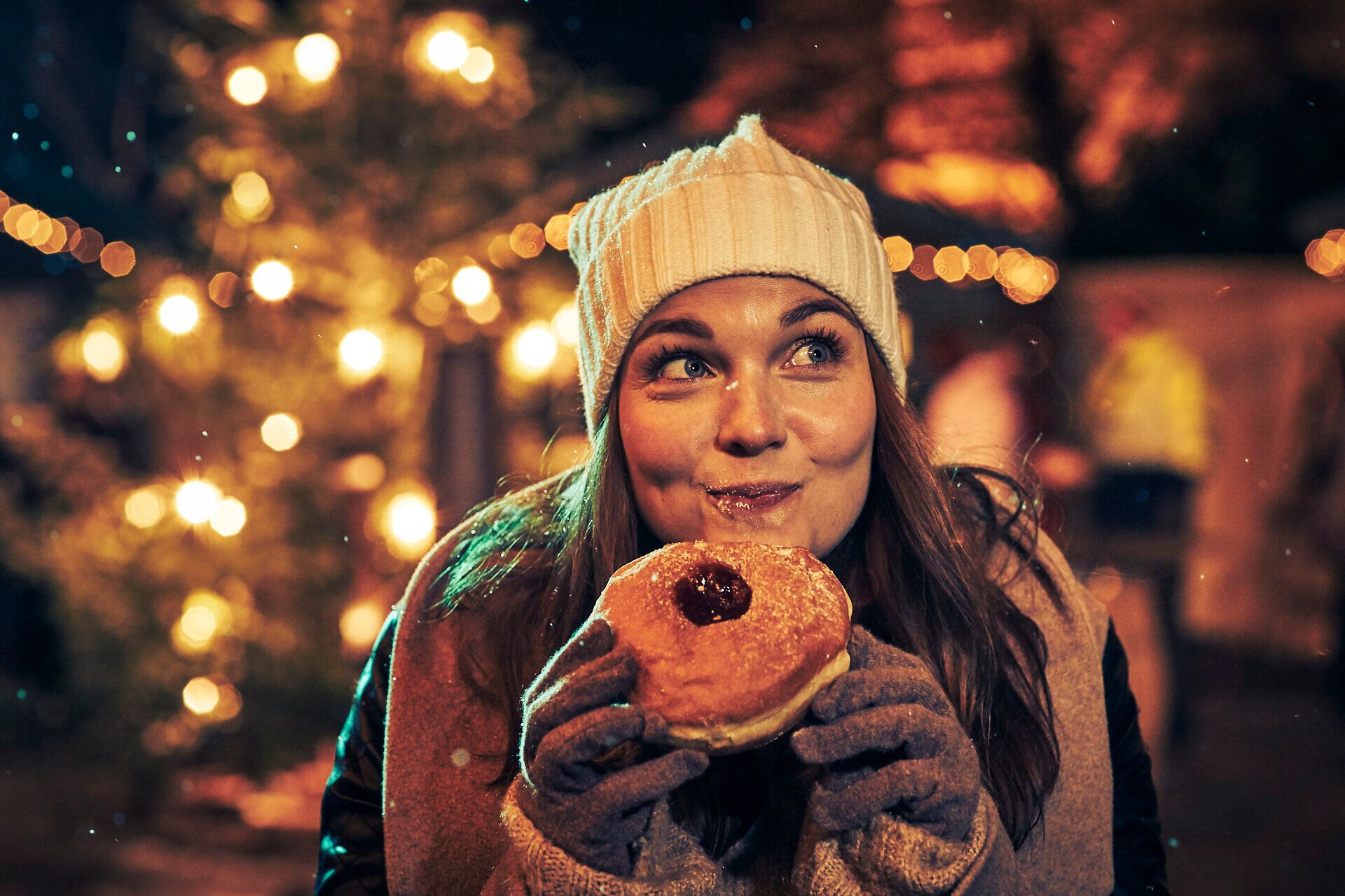 Inmitten der festlichen Lichter strahlt die Freude der Winterzeit. Eine fröhliche Person genießt einen köstlichen Krapfen, während der Duft von frisch gebrannten Mandeln in der Luft liegt. Die winterliche Atmosphäre lädt dazu ein, die Magie der Saison zu erleben.
