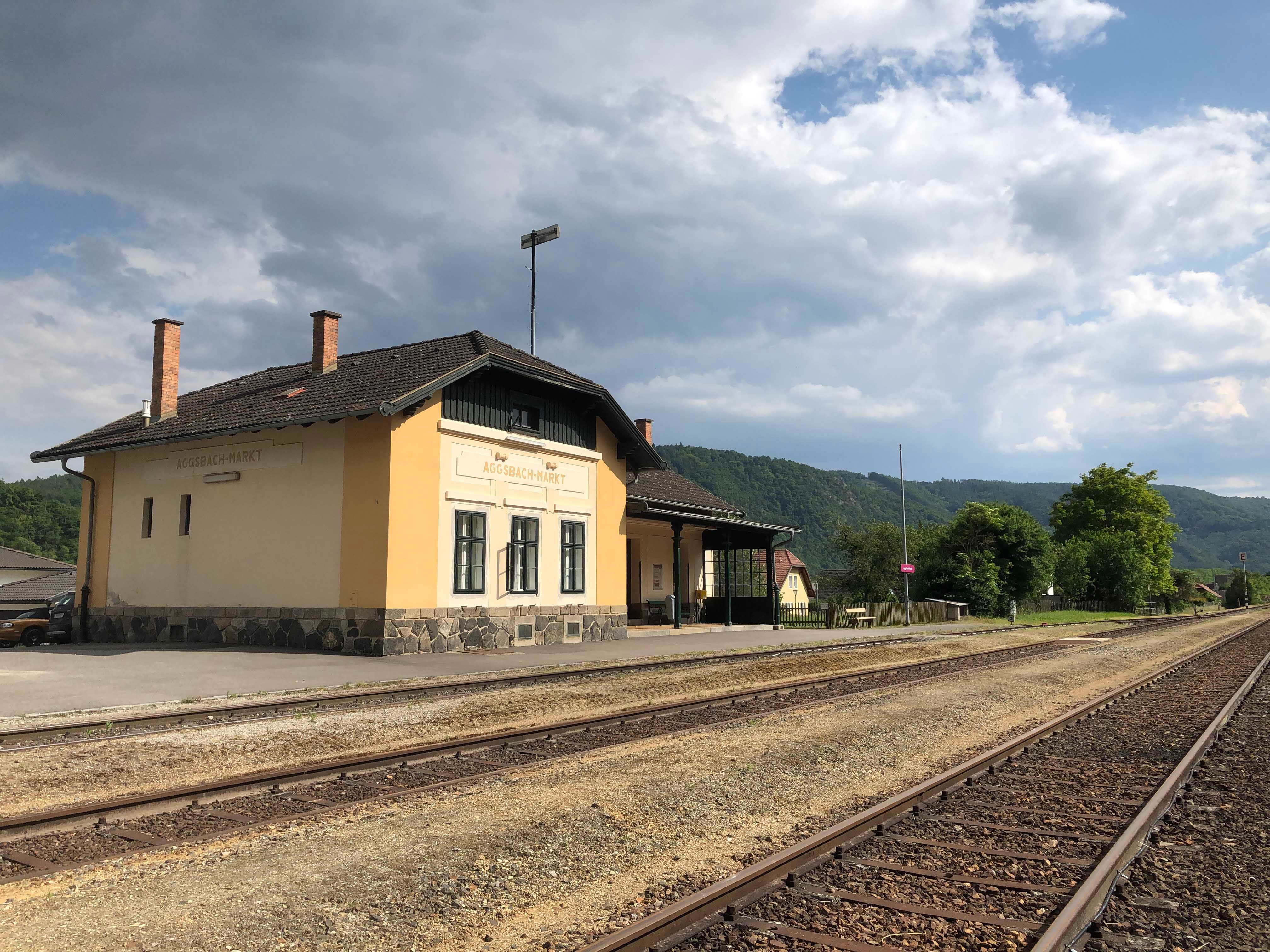 Bahnhof Aggsbach-Markt mit Gleisen und bewölktem Himmel.
