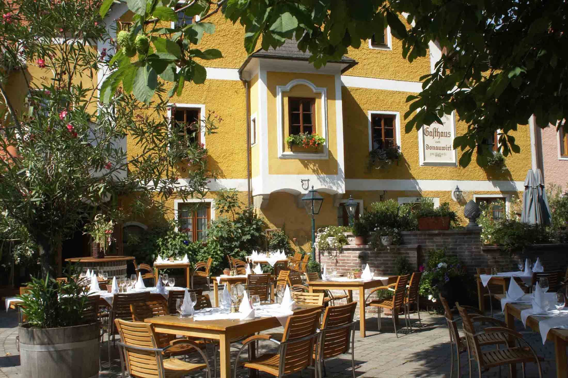 Terrasse eines Gasthauses mit gedeckten Tischen und Pflanzen.