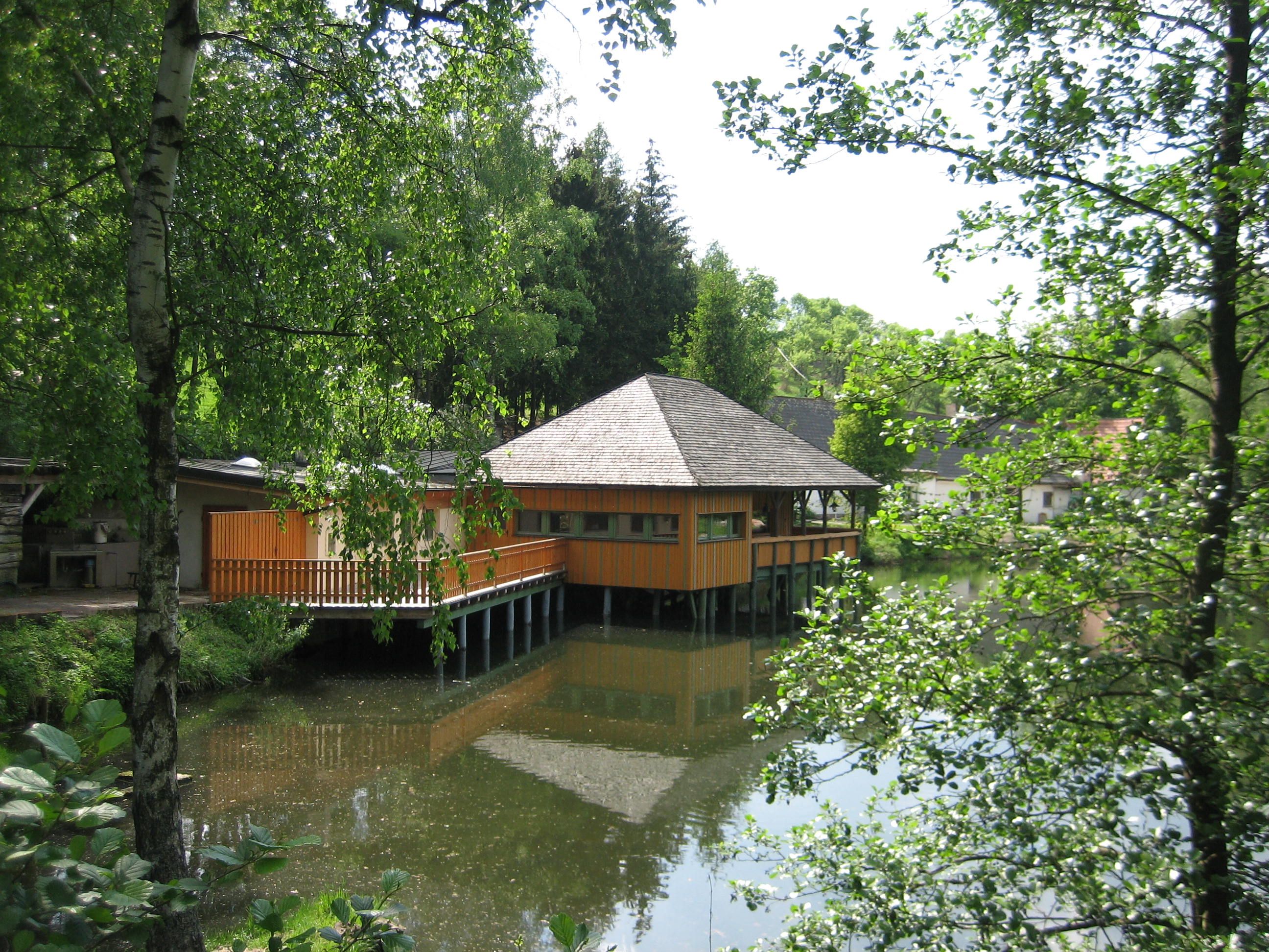 Ein Holzgebäude auf Stelzen über einem Teich, umgeben von Bäumen.