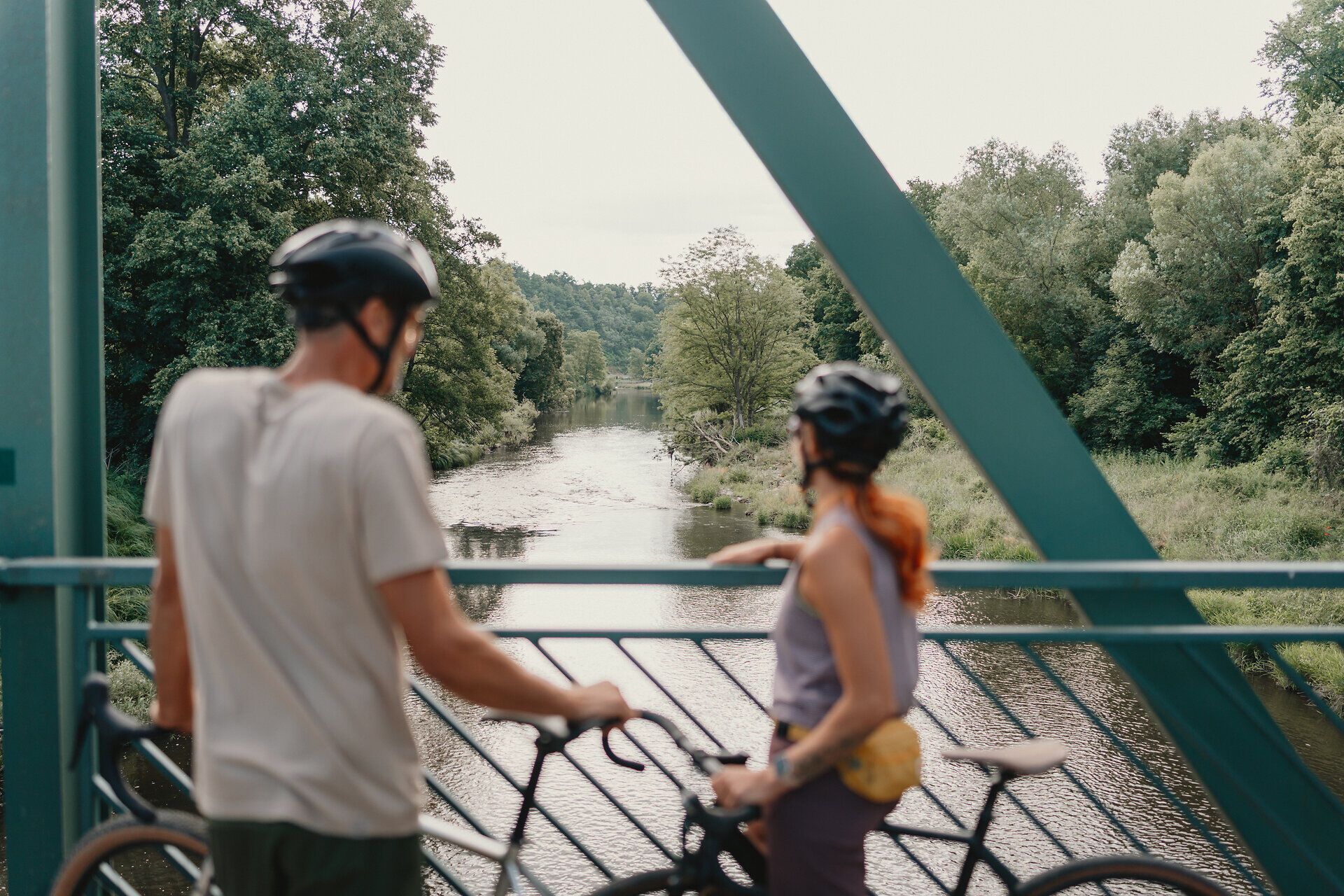 Zwei Radfahrende blicken von einer Brücke bei Schloss Buchberg auf den Kamp im Waldviertel.