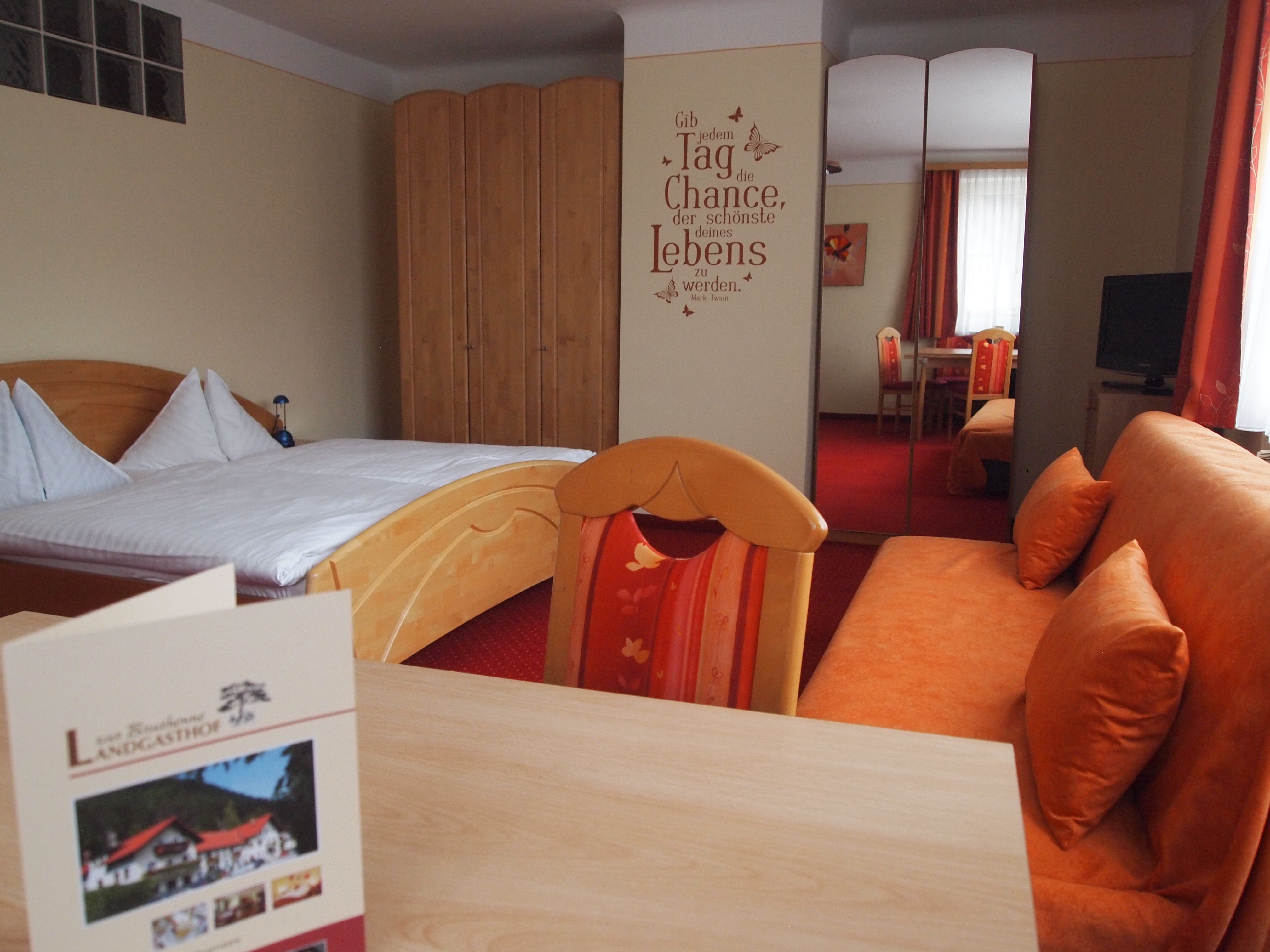 Ein gemütliches Hotelzimmer mit einem Doppelbett, einem Sofa, einem Tisch und einem Schrank. An der Wand steht ein motivierender Spruch.