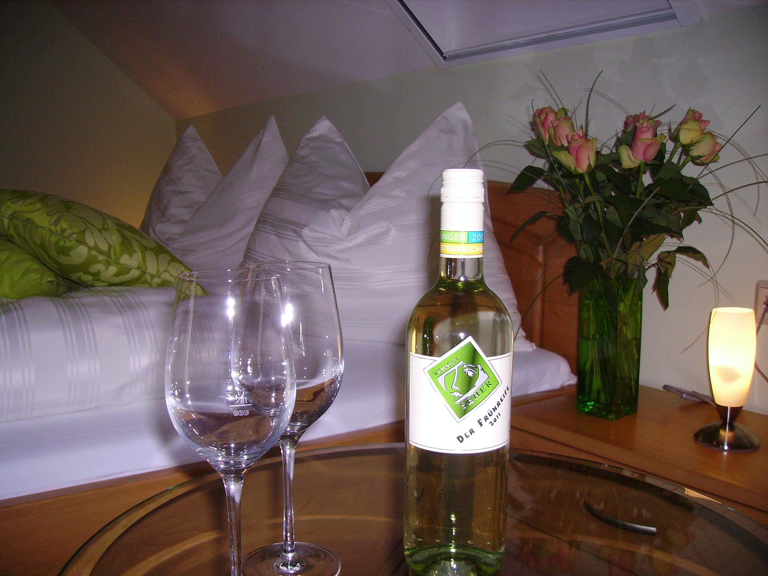 Ein gemütliches Gästezimmer mit einer Flasche Wein, zwei Gläsern und einem Blumenstrauß auf einem Tisch.
