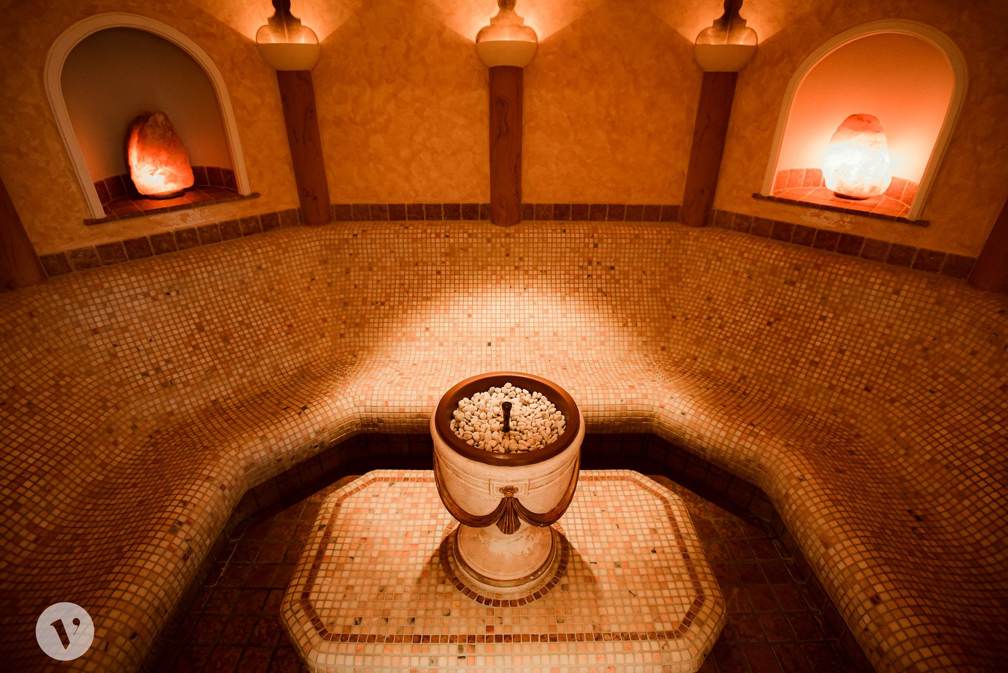 Ein Laconium mit Mosaikfliesen, einem zentralen Brunnen und warmem Licht.