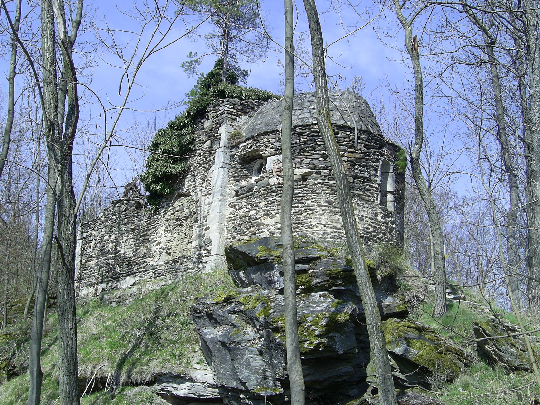 Ruine in einem Wald mit Bäumen und blauem Himmel.