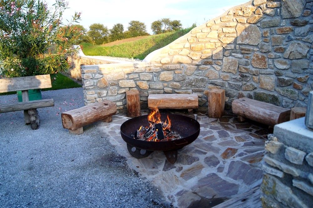 Grillplatz mit Feuerstelle und Holzbänken vor einer Steinmauer.