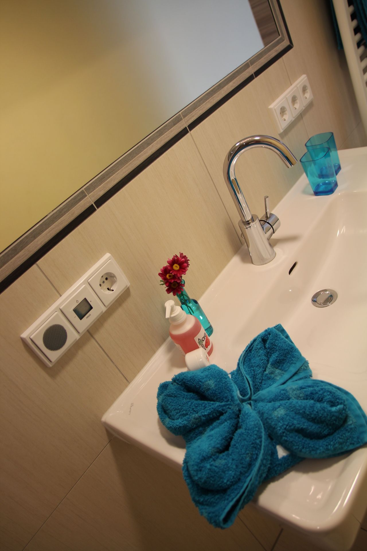 Waschbecken mit blauem Handtuch, Seifenspender und Vase mit Blumen.