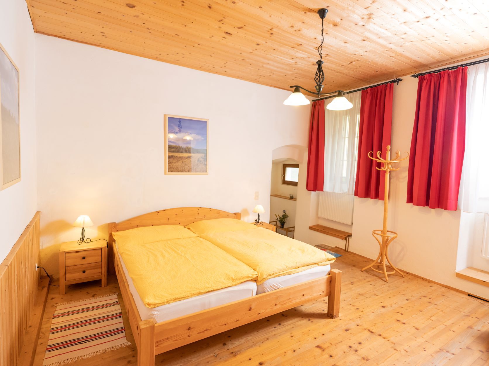 Gemütliches Schlafzimmer mit Holzmöbeln, gelber Bettwäsche und roten Vorhängen.