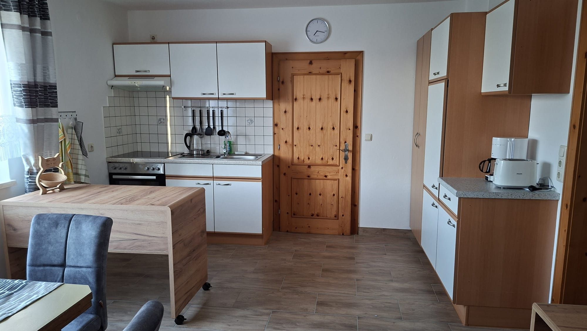 Moderne Küche mit Holz- und weißen Elementen, Esstisch, Stühlen und Küchengeräten.