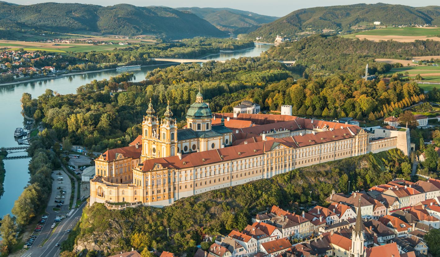 Luftaufnahme des Stifts Melk in Österreich, umgeben von grüner Landschaft und der Donau.