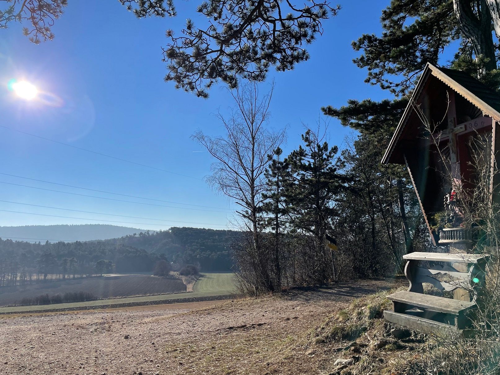 Landschaft mit Hütte und Bäumen bei Sonnenschein.