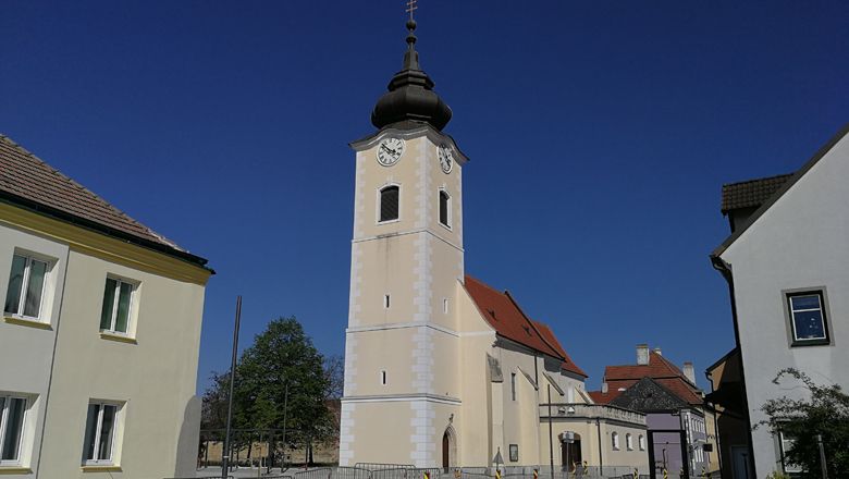 Kirche mit Turm und Uhr in Rohrendorf vor blauem Himmel.
