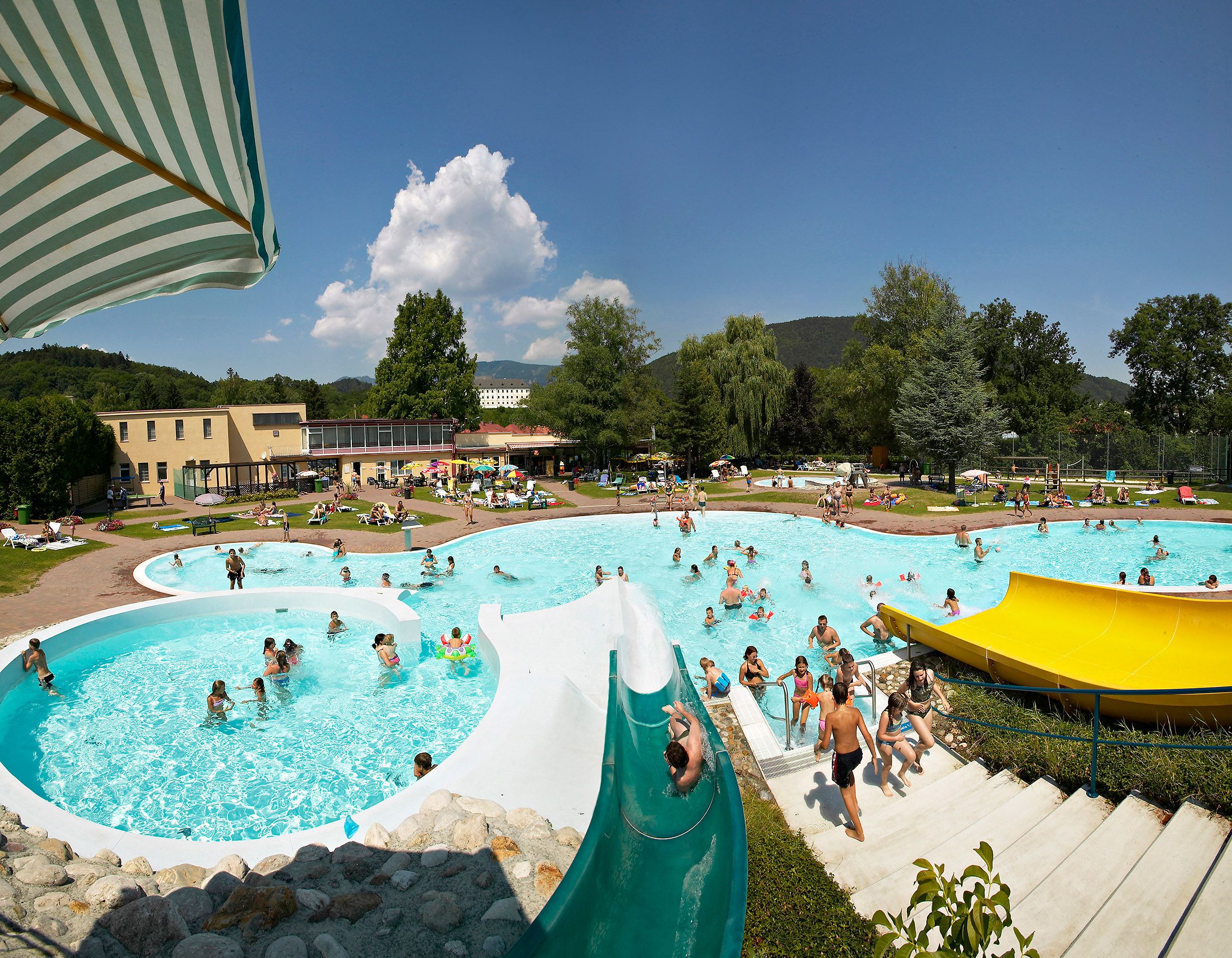 Ein Freibad mit mehreren Pools, Wasserrutschen und vielen Menschen an einem sonnigen Tag.