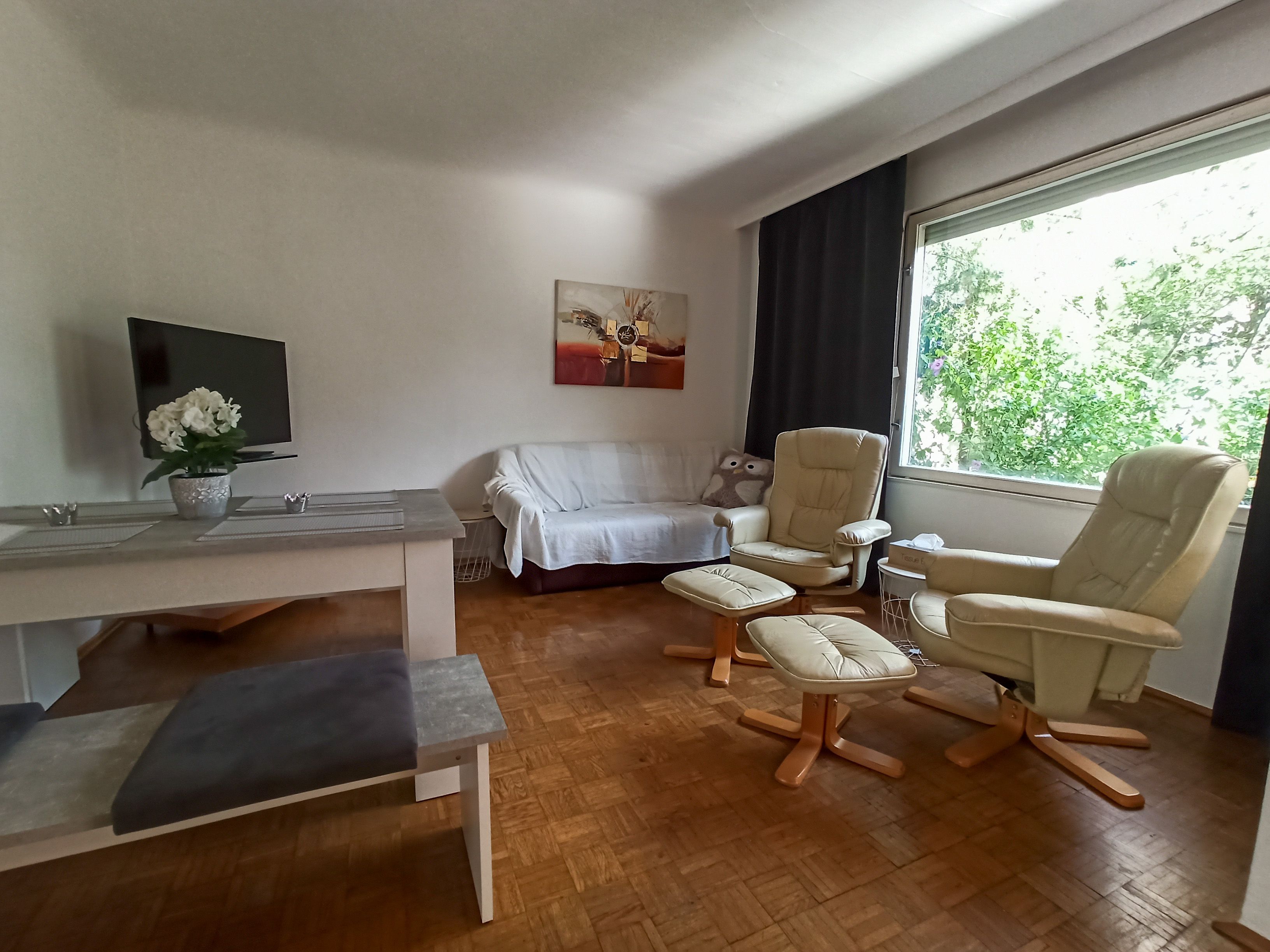 Wohnzimmer mit Sofa, zwei Sesseln, Tisch und großem Fenster.