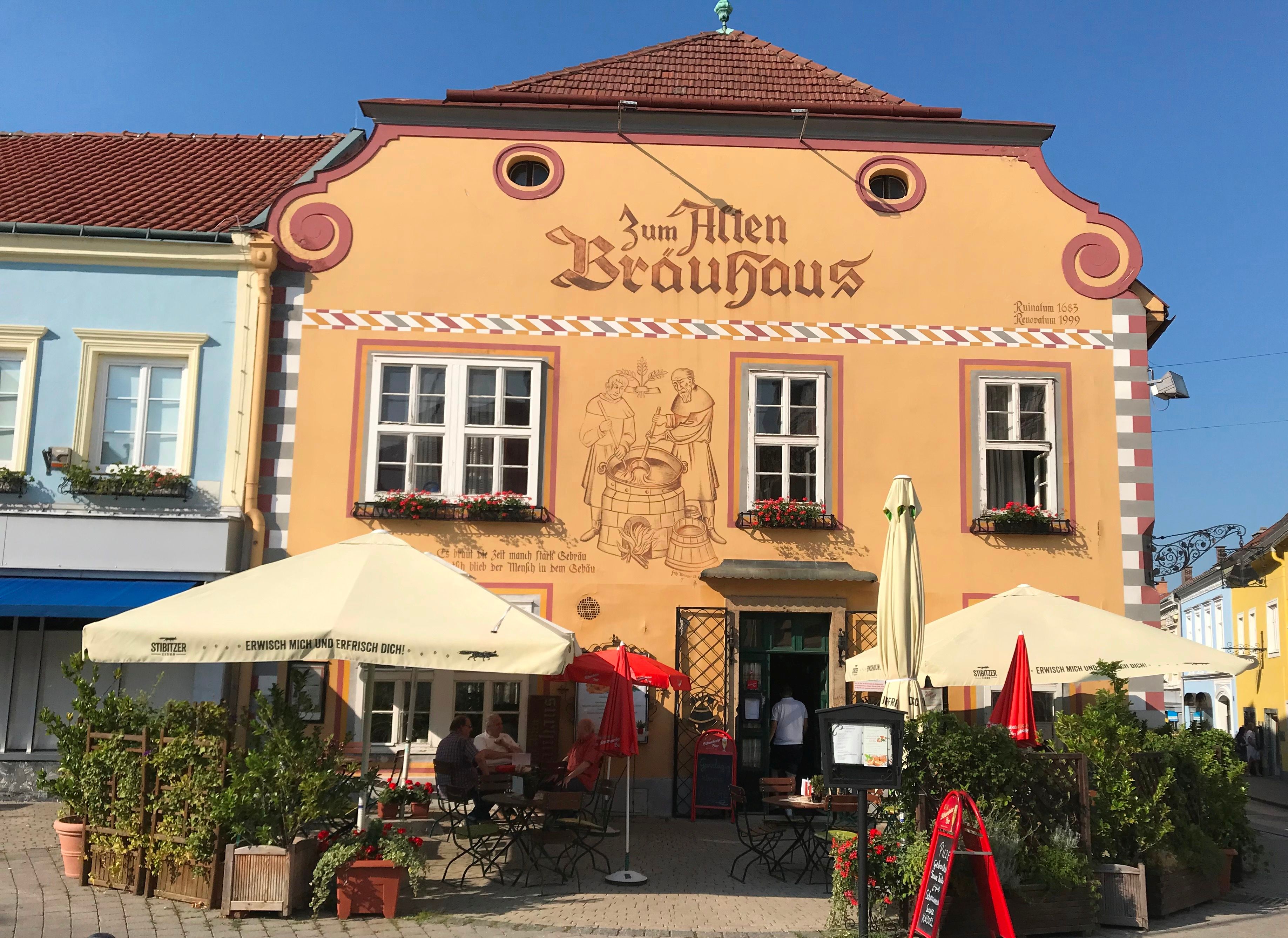 Fassade eines traditionellen Brauhauses mit Sonnenschirmen und Sitzbereich im Freien.