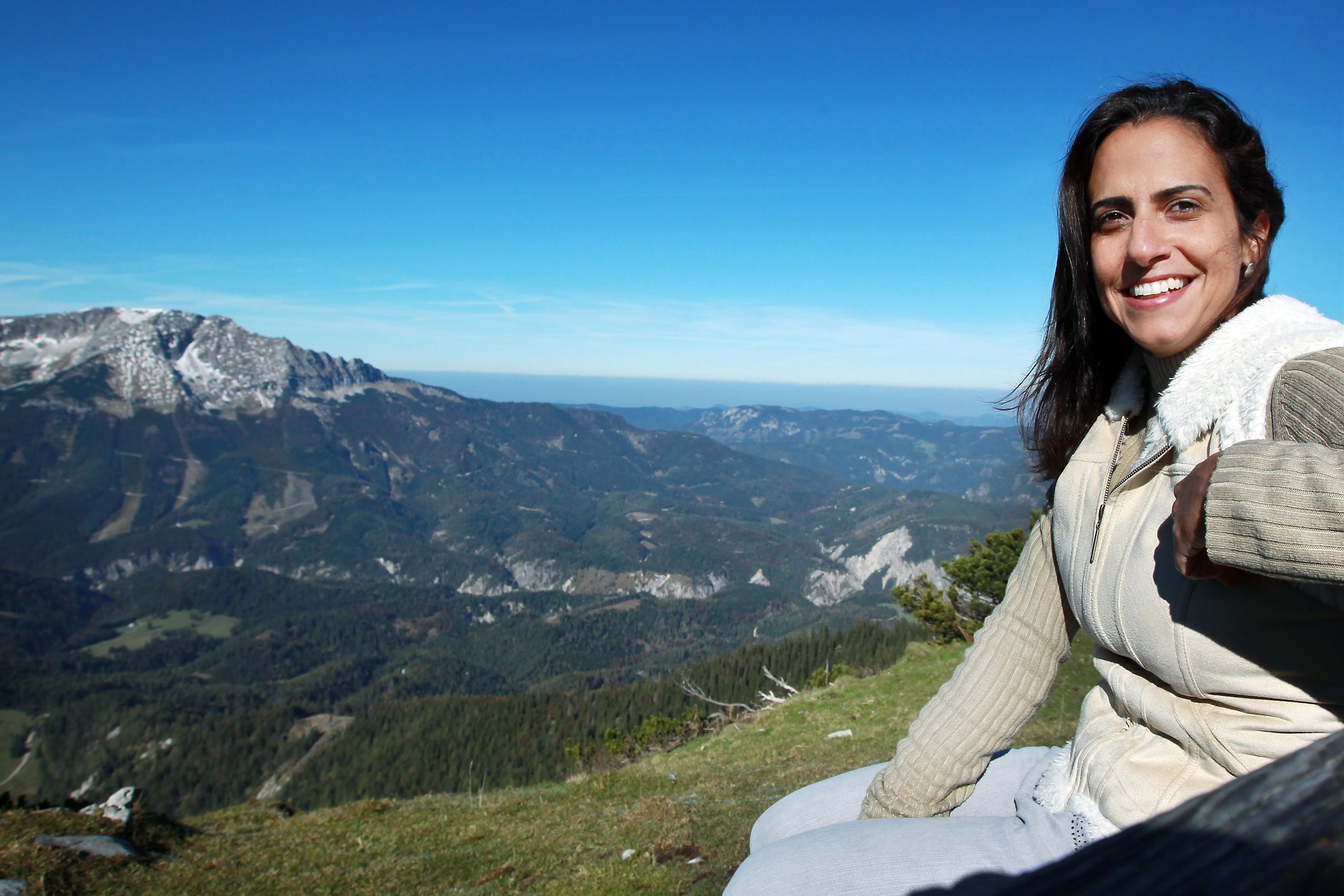 Frau sitzt auf einem Berg mit Blick auf eine Berglandschaft.