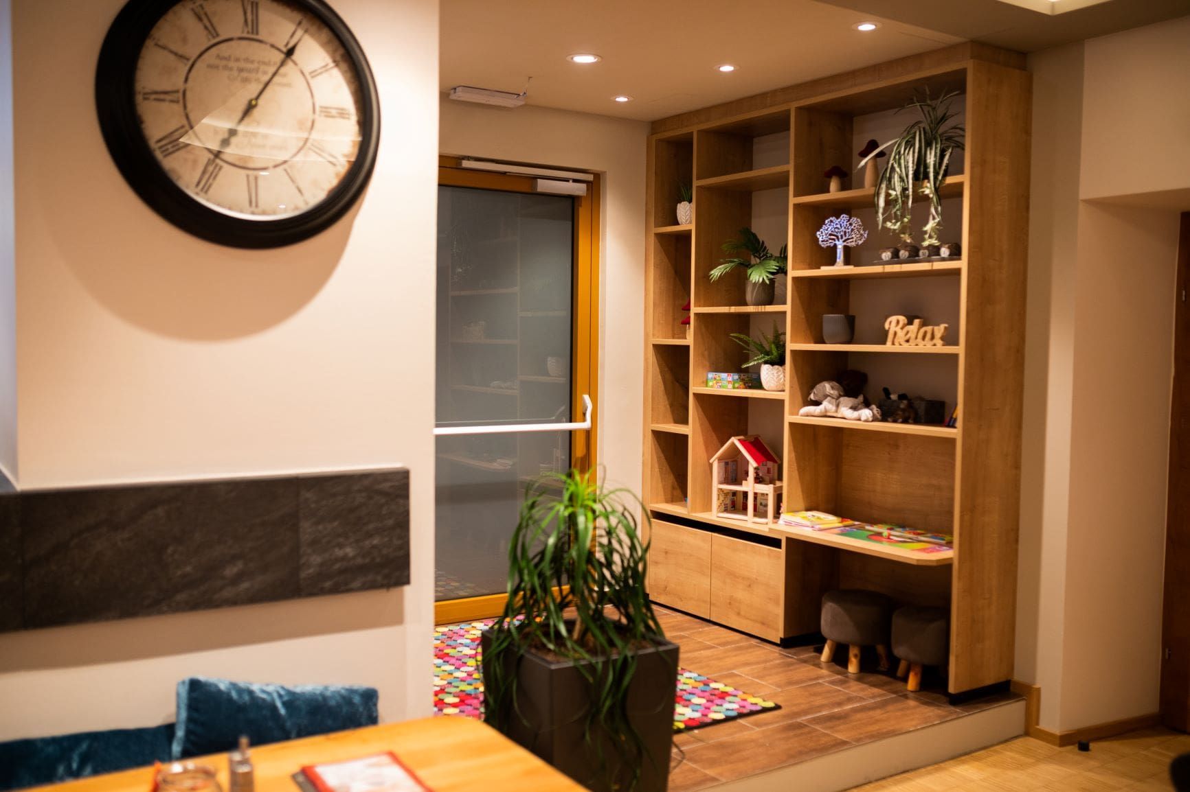 Innenansicht eines Bistros mit großer dekorativer Uhr, Regal und Kinderspielecke.