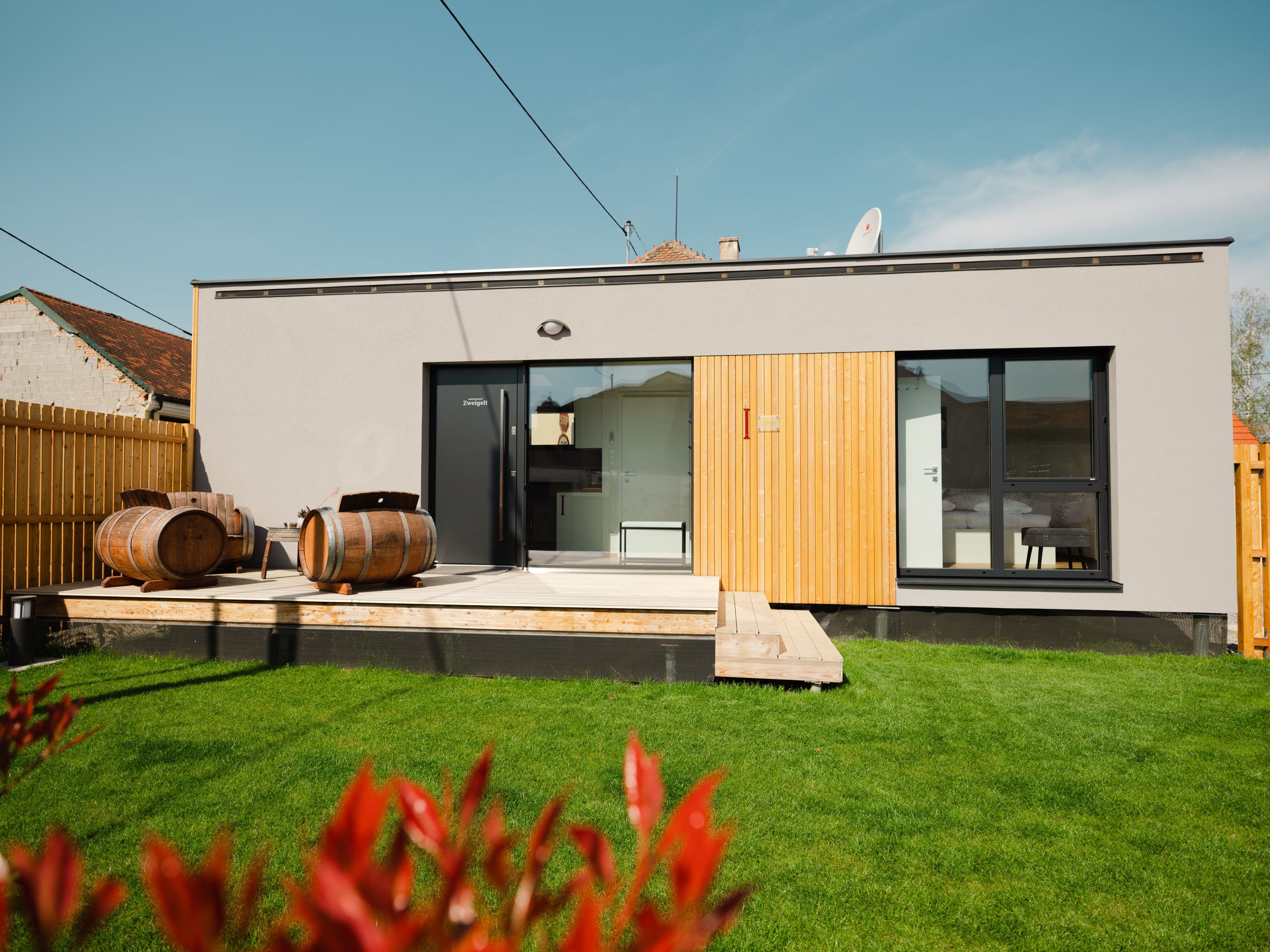 Modernes Gebäude mit Terrasse und Weinfässern im Garten.
