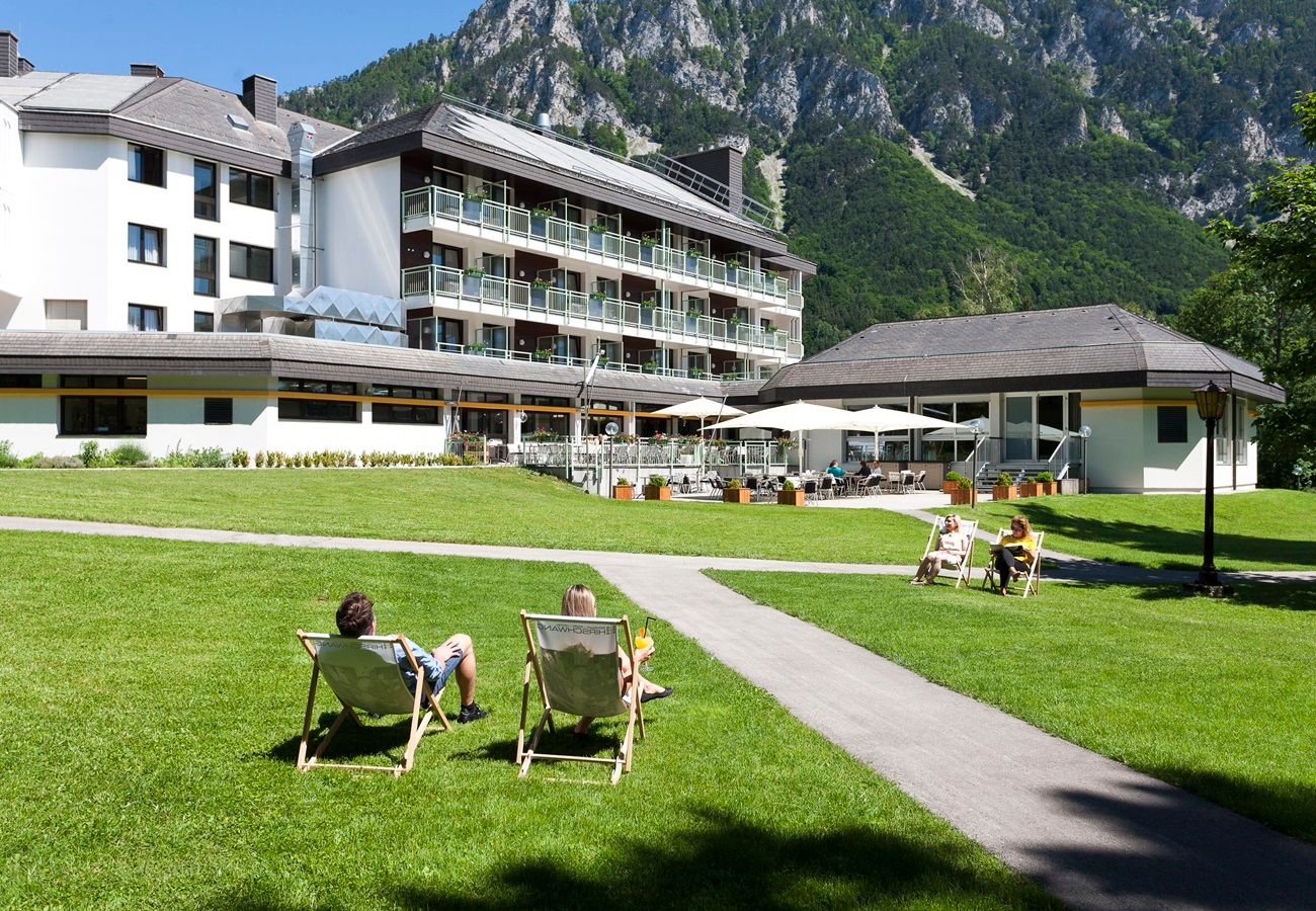Ein Hotel mit Terrasse und Liegestühlen auf einer Wiese, umgeben von Bergen.