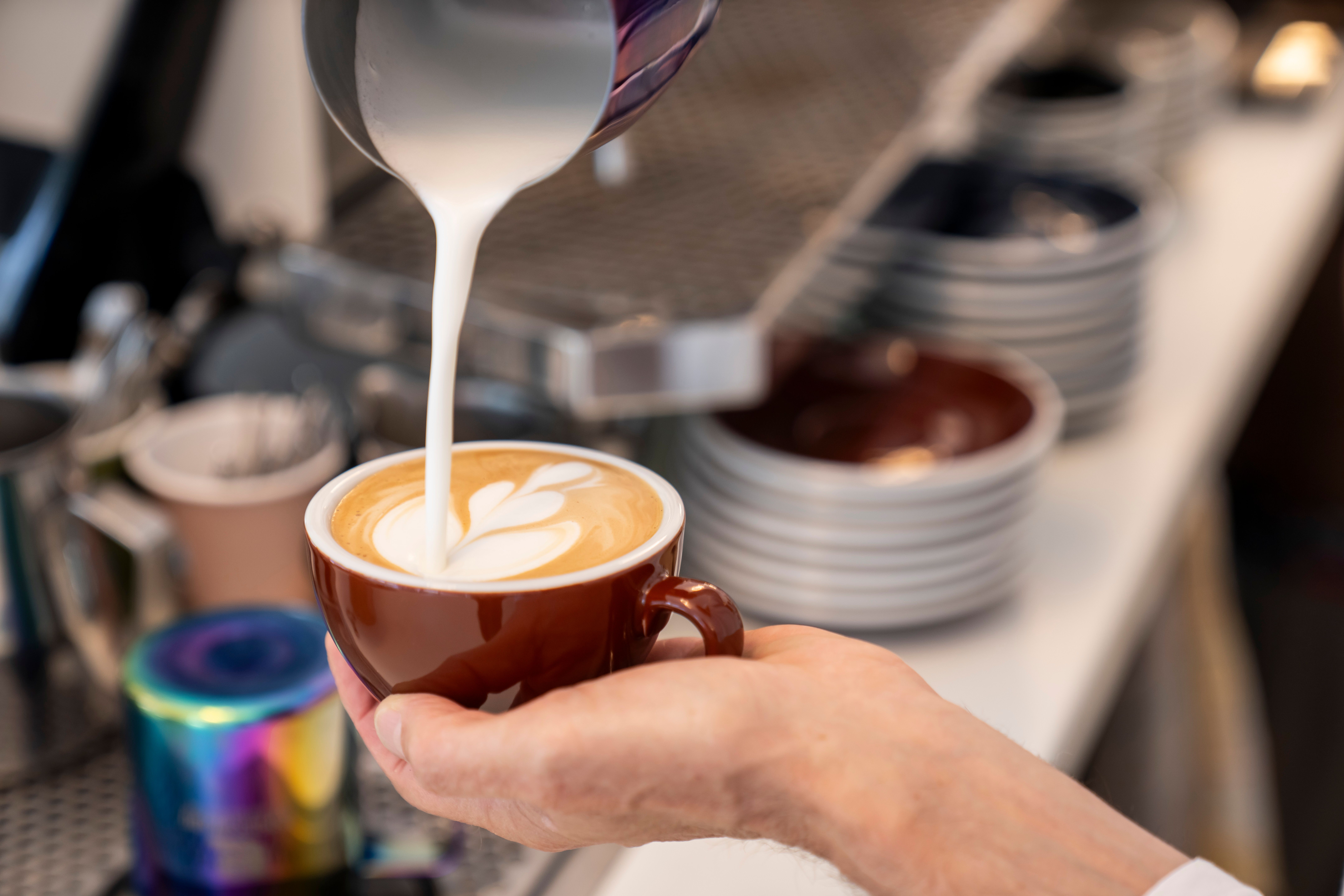 Nahaufnahme einer Hand, die Latte Art in einer Kaffeetasse gießt.