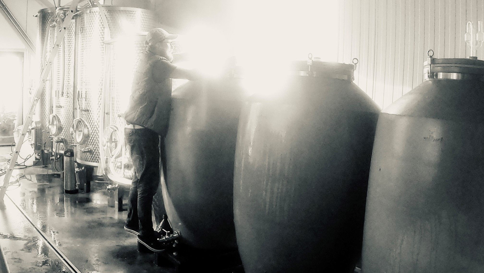 Person arbeitet in einer Weinkellerei mit großen Tanks.